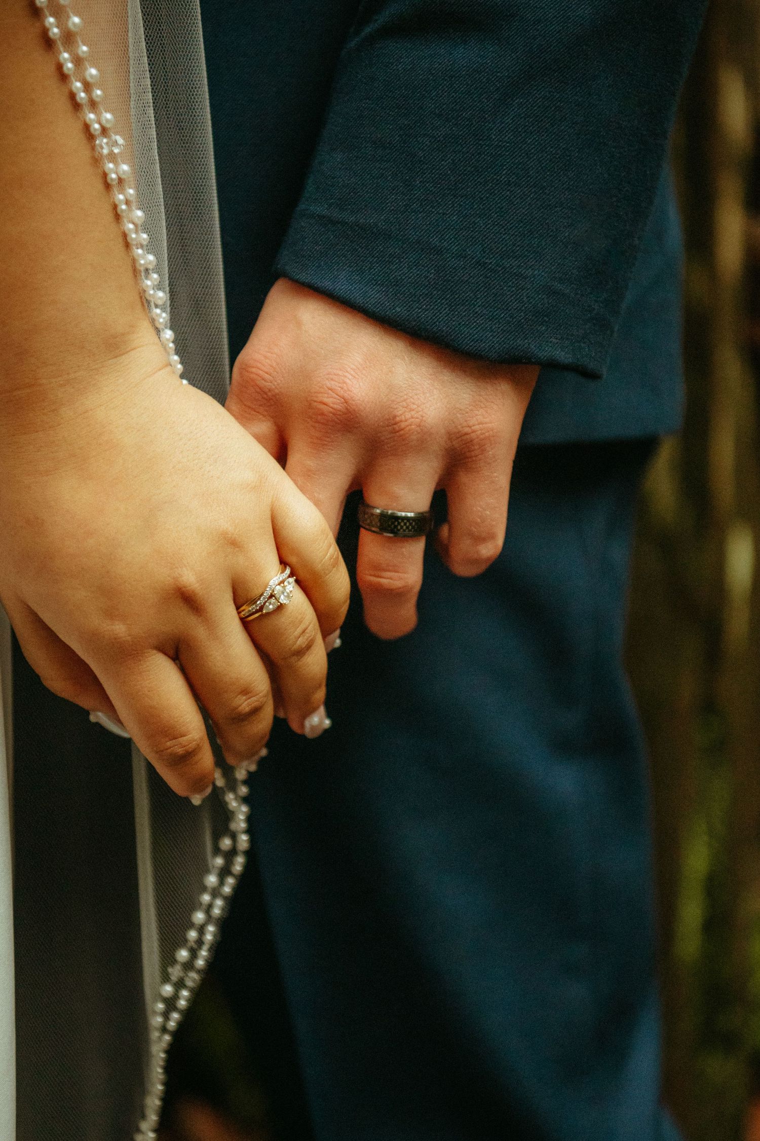 Close-up shot of couple's hands wearing wedding rings with a sparkly dress detail in view.