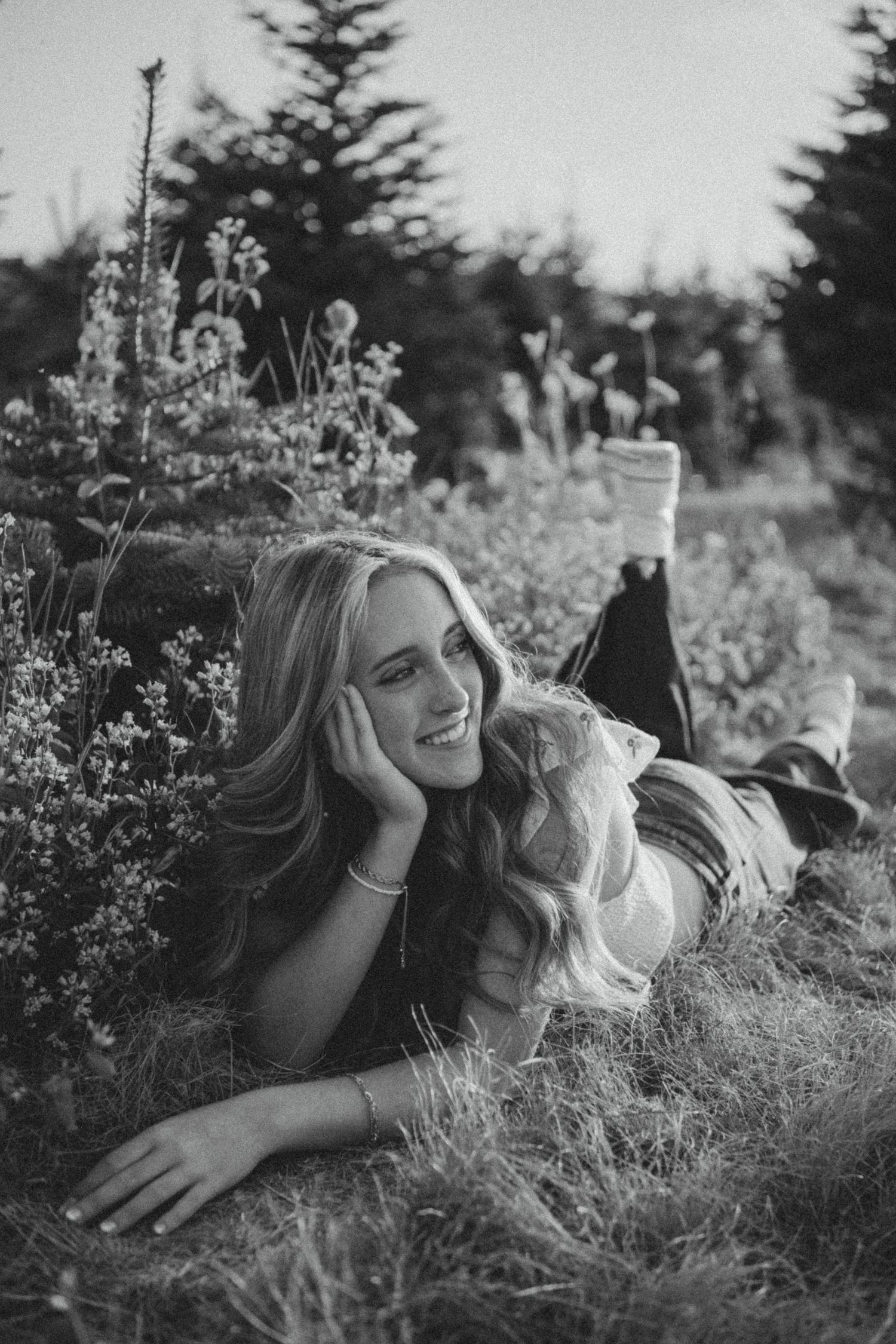 Black and white portrait of someone laying in tall grass and wildflowers in a natural outdoor setting.