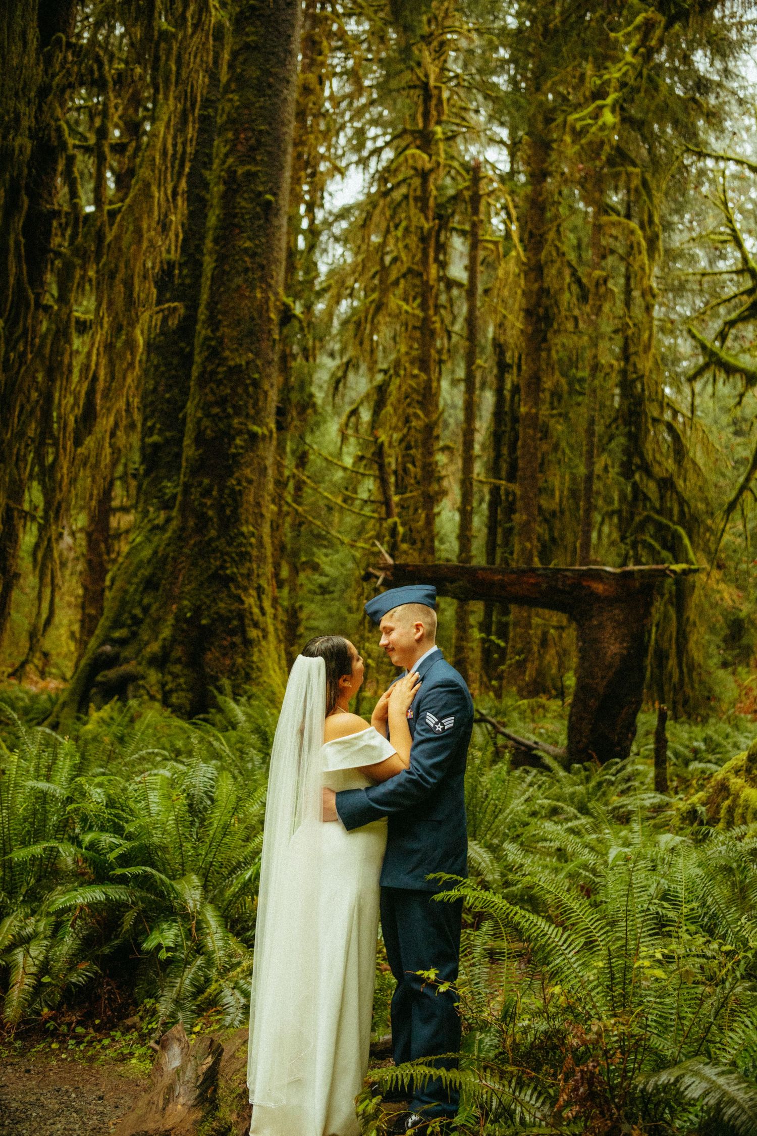 A couple embraces during their wedding ceremony in a lush Pacific Northwest forest surrounded by towering trees and ferns.