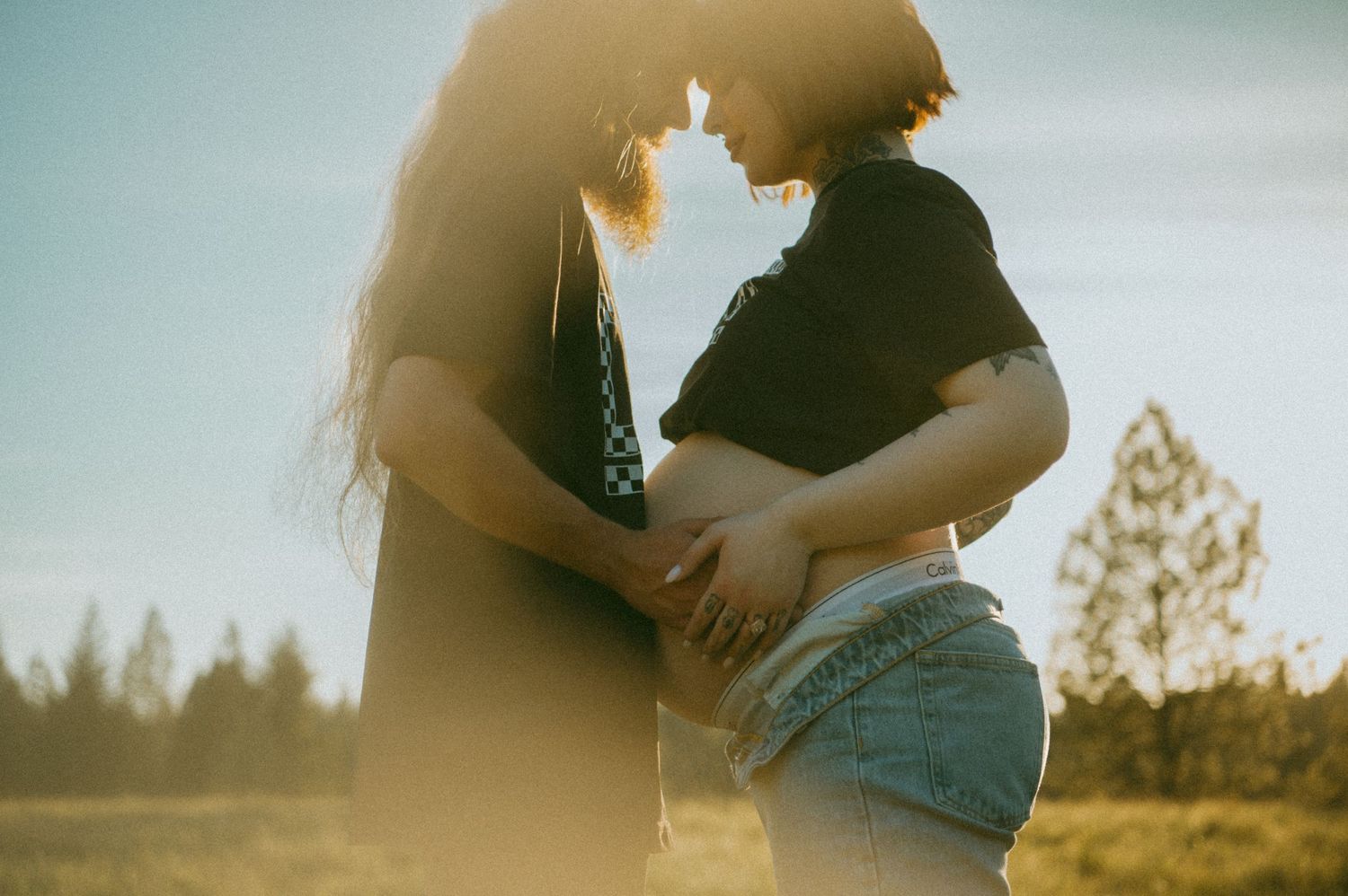 A romantic silhouette of a couple embracing in soft golden sunlight with trees in the background.