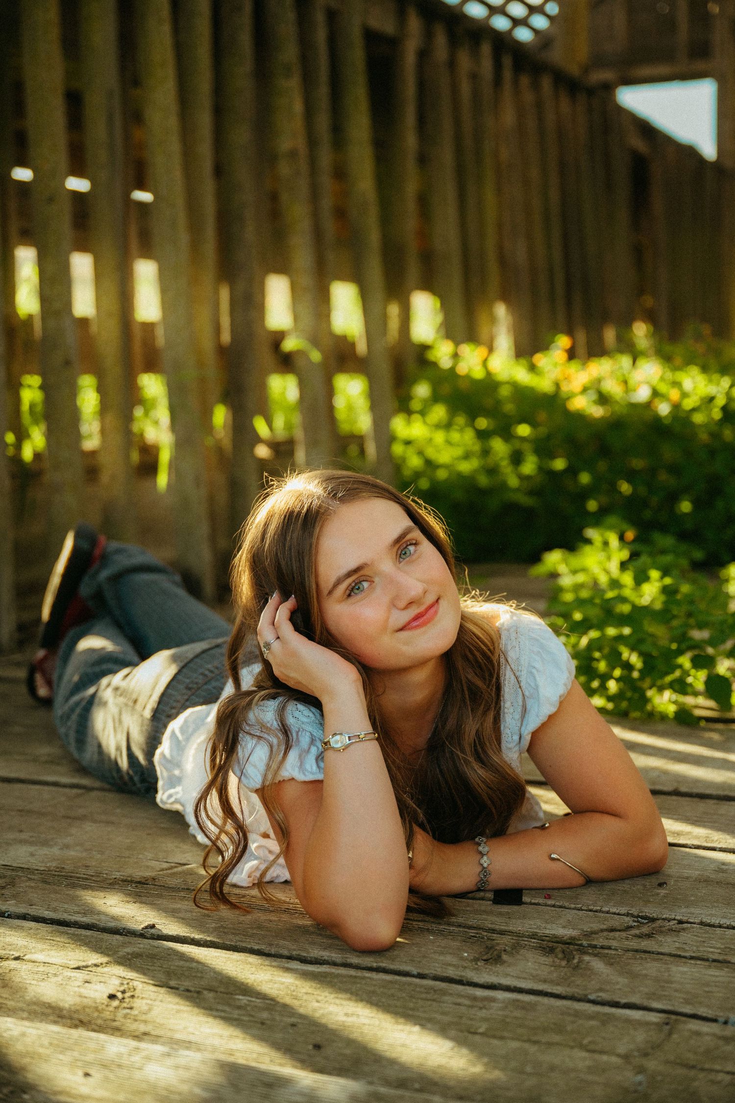 A person in casual attire lies on a wooden deck during golden hour as sunlight filters through wooden slats.