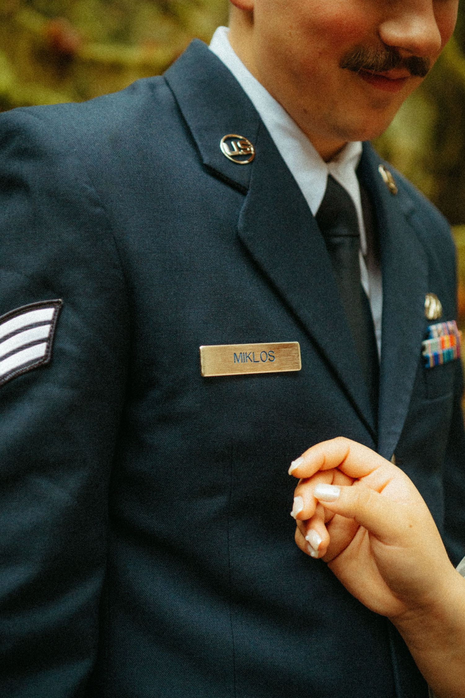 Someone's hand adjusts a military uniform with service stripes and a name tag on a dress blue jacket.
