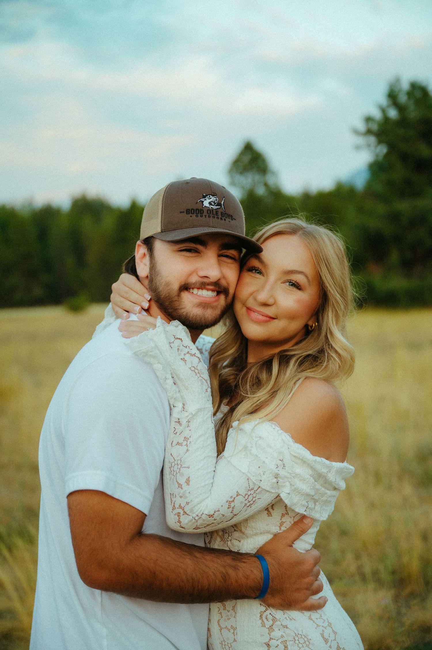 A couple embraces in a sunlit field wearing white outfits during a romantic outdoor photoshoot.