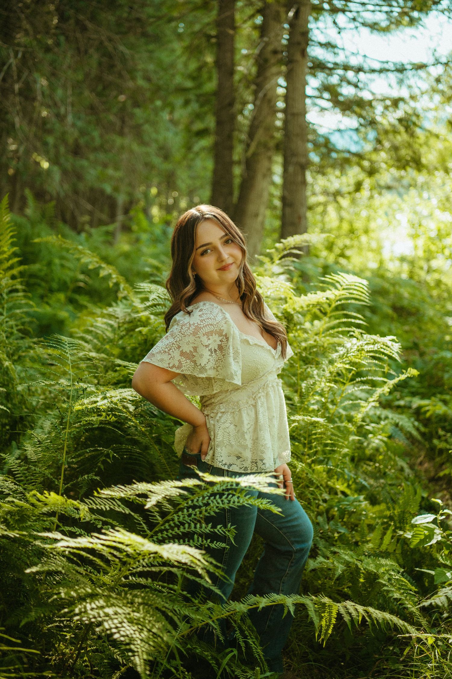 A dreamy forest photoshoot among lush green ferns with sunlight filtering through the trees creating a magical atmosphere.