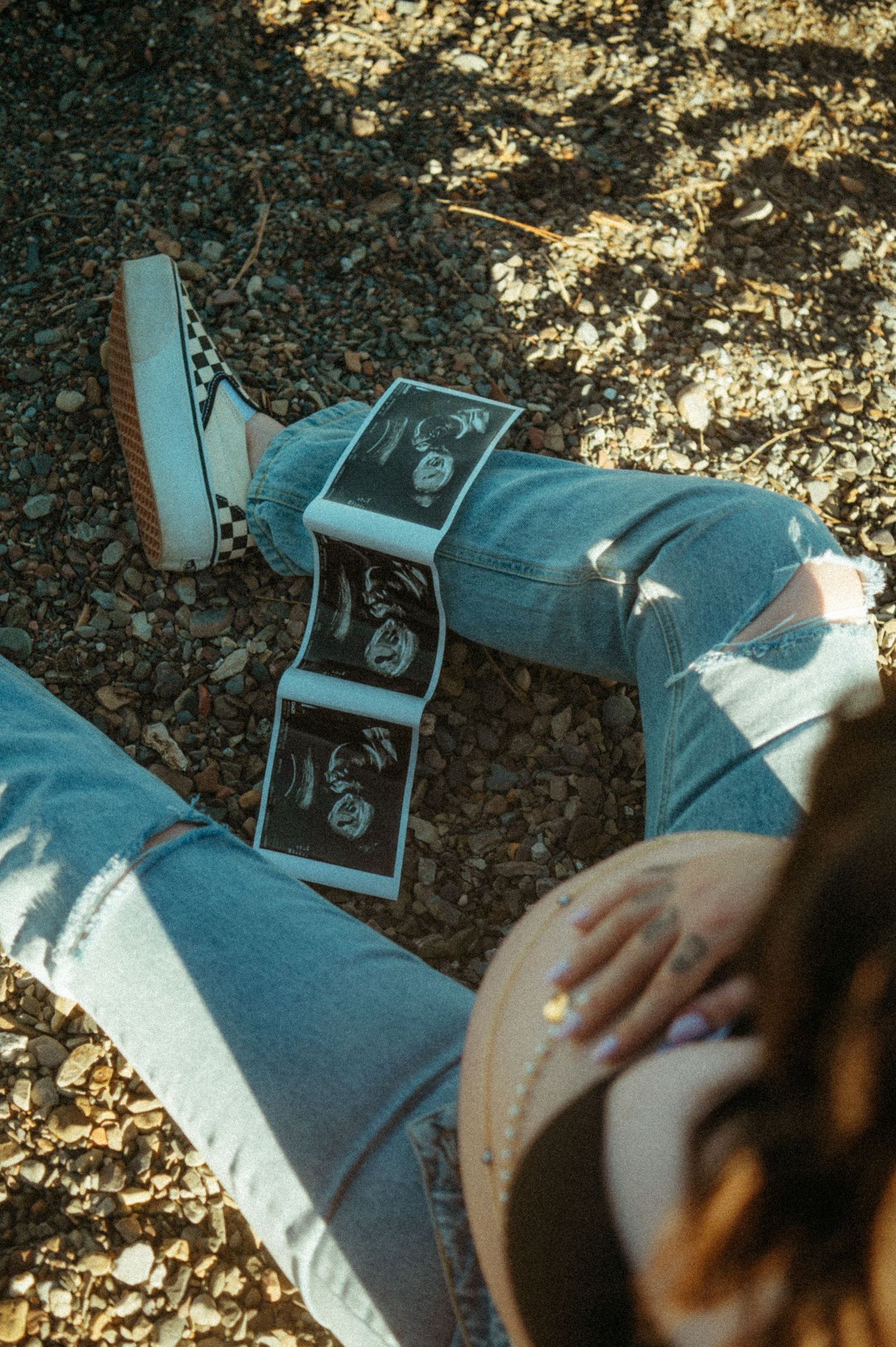 Ultrasound sonogram photos displayed on lap while sitting outdoors in blue jeans on fallen leaves.