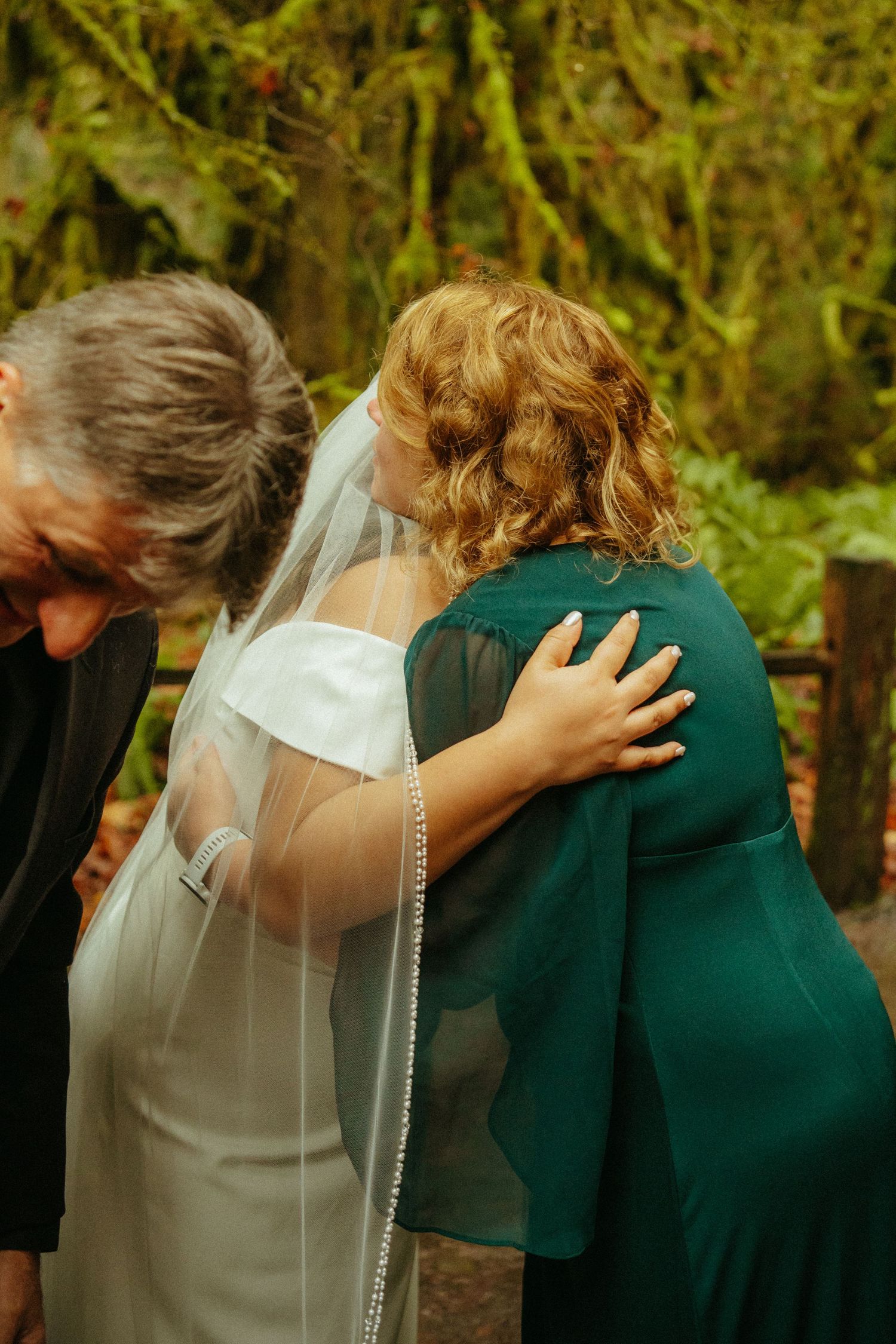 An emotional moment is shared between a bride in white and someone wearing a green dress during a wedding ceremony outdoors.