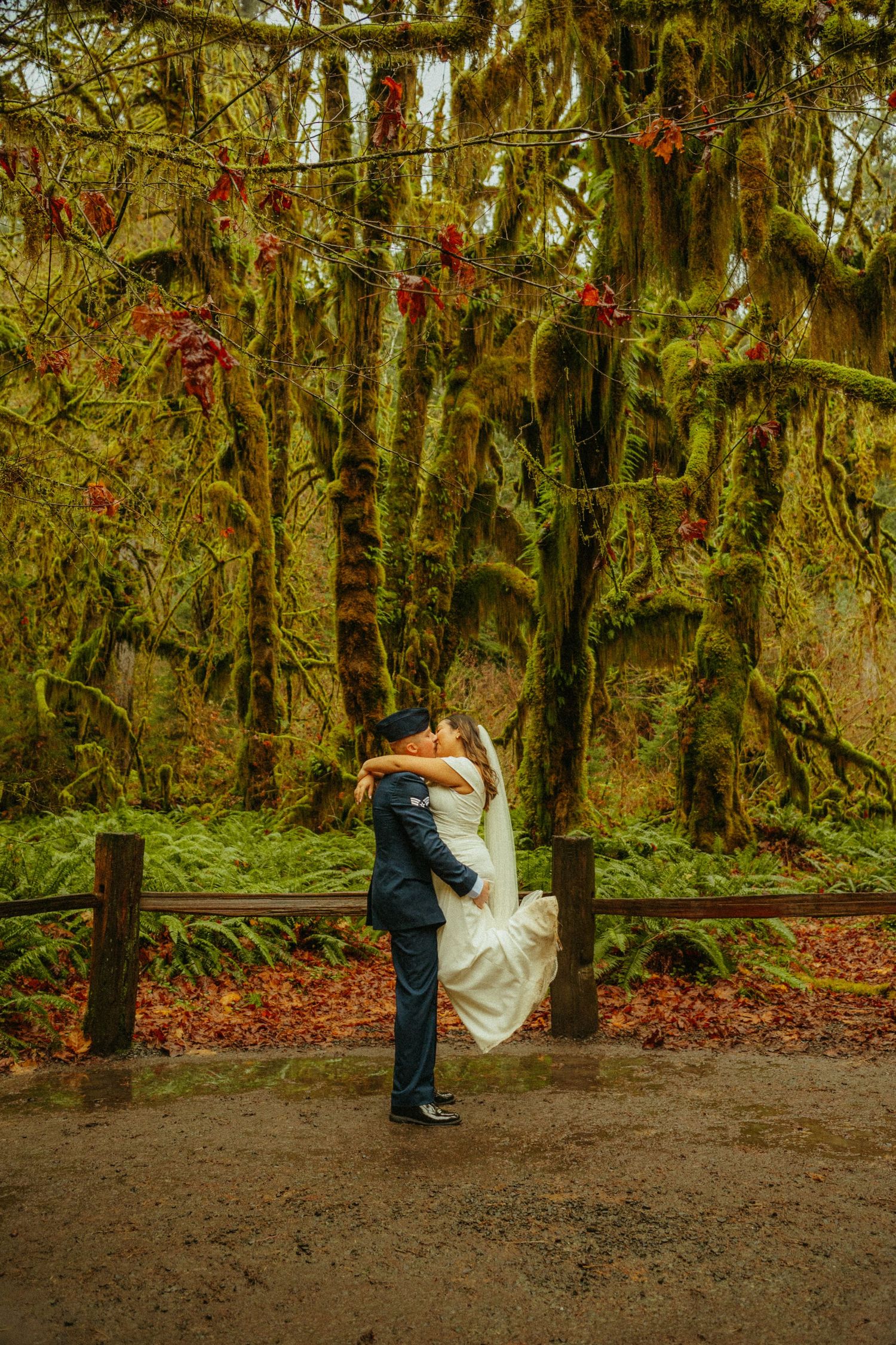 A romantic embrace in front of mossy trees in an enchanting Pacific Northwest forest.