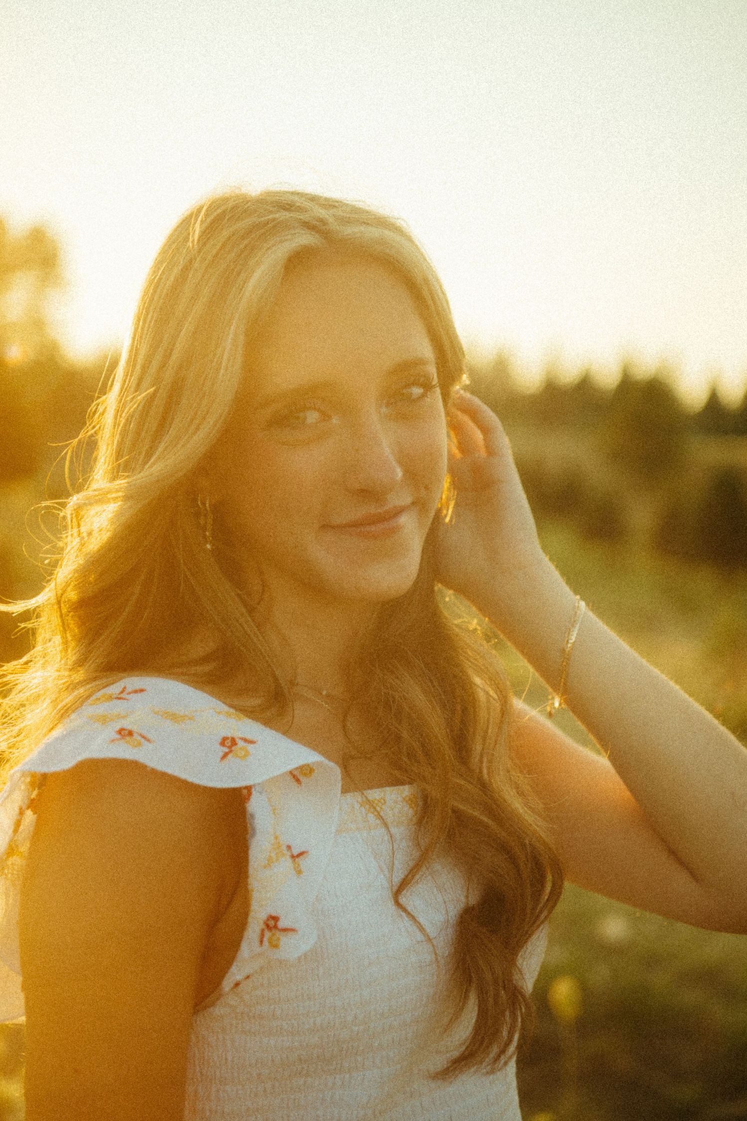 A portrait photograph captures a person in a white floral dress against a golden sunset backdrop outdoors.