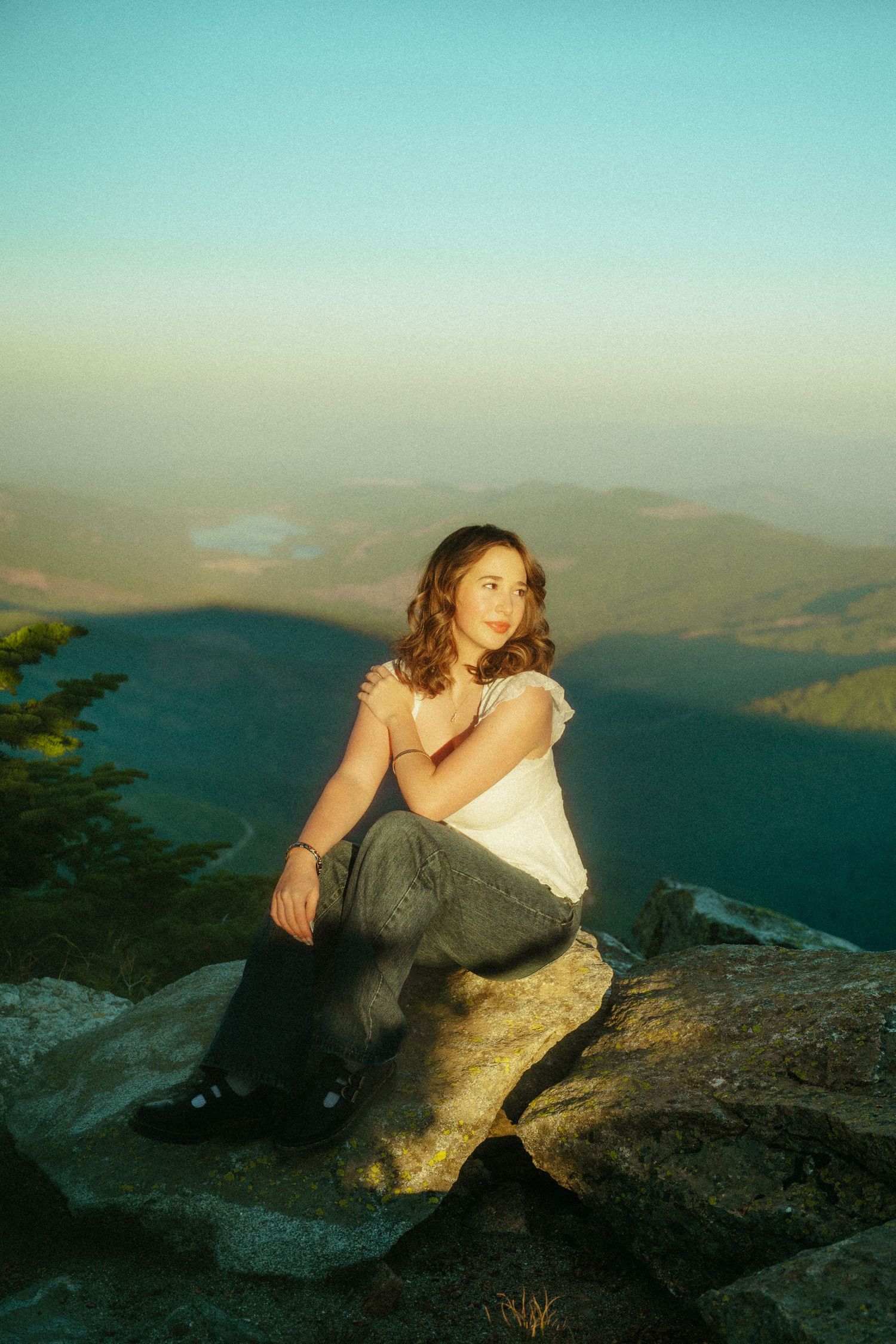 Person reclining on rocky mountain summit at sunset with scenic valley and mountain views in the background.