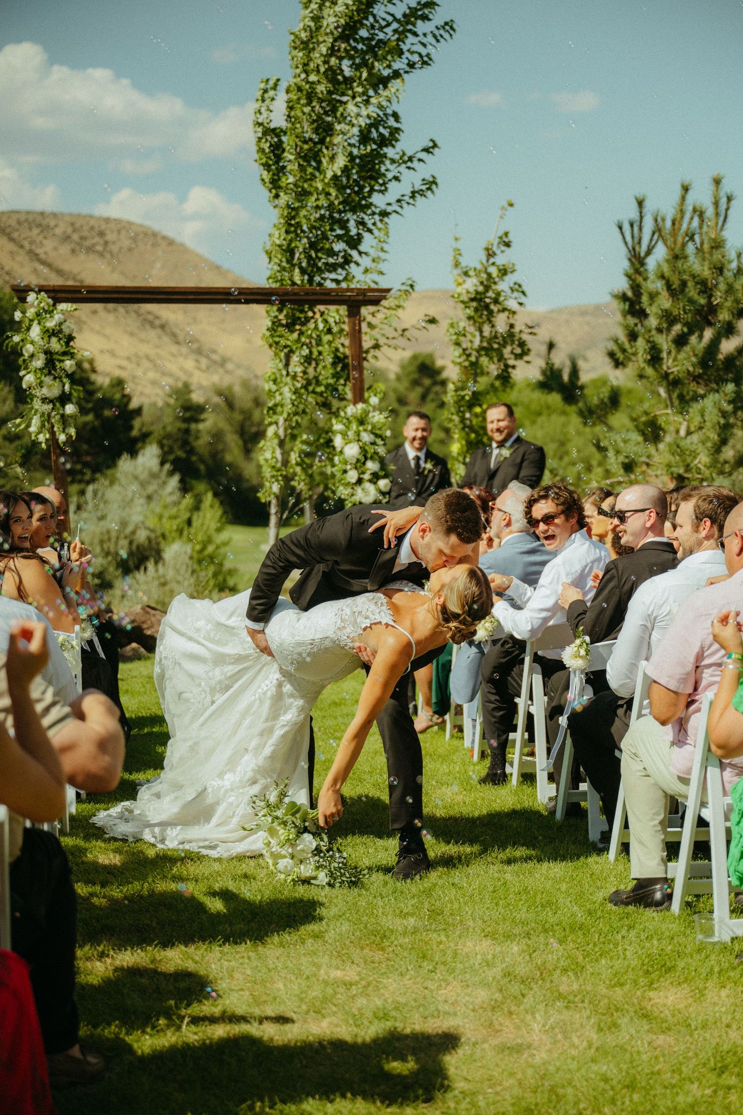 A sequence of wedding guests dramatically falling over like dominos on a grassy lawn during an outdoor ceremony.