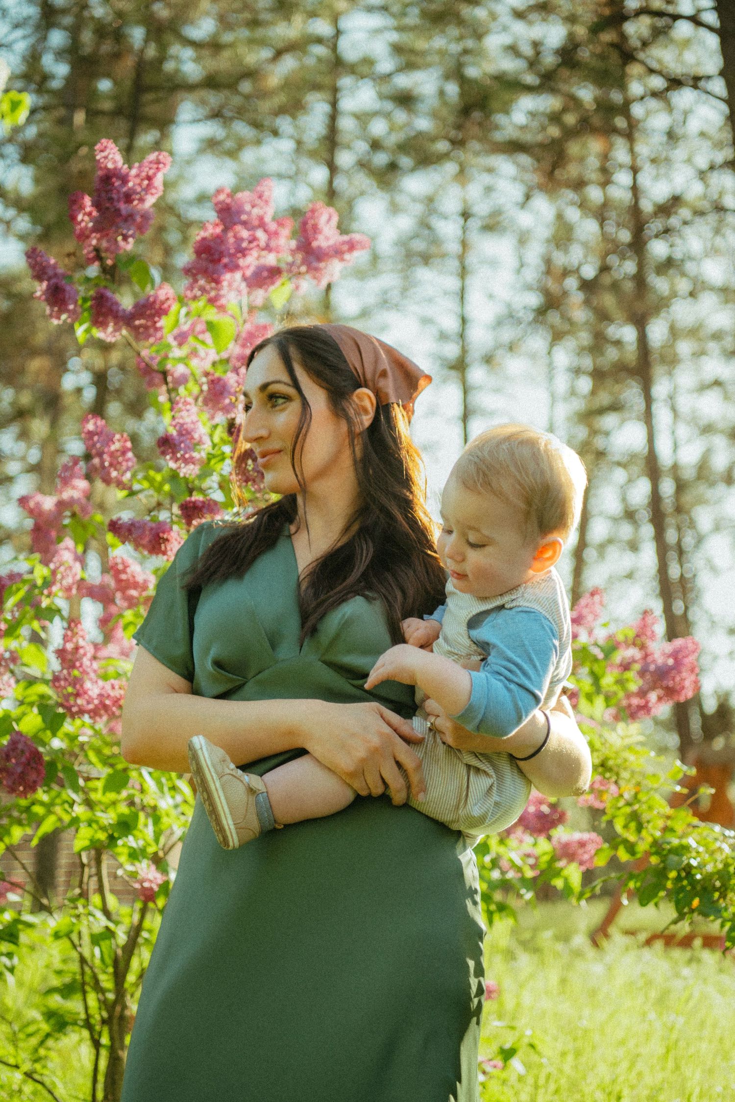 A tender moment shared between parent and child amid blooming pink lilacs in a sunlit forest setting.