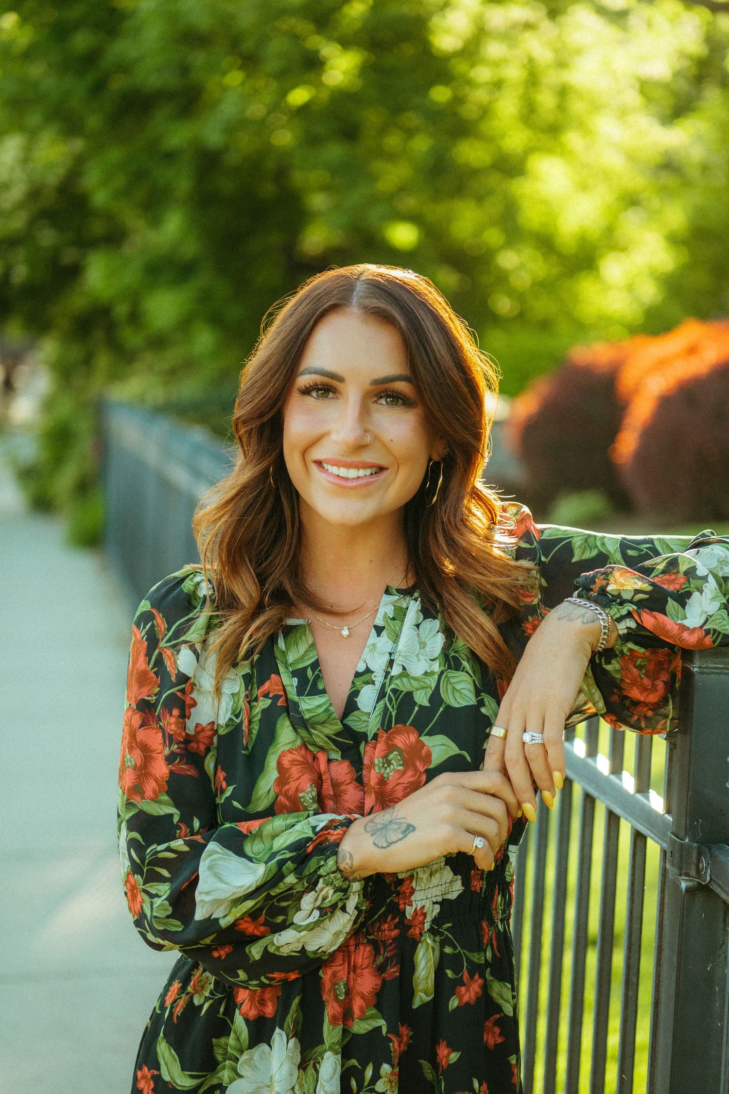 A floral dress in green and orange tones is worn outdoors in a sunlit garden setting.