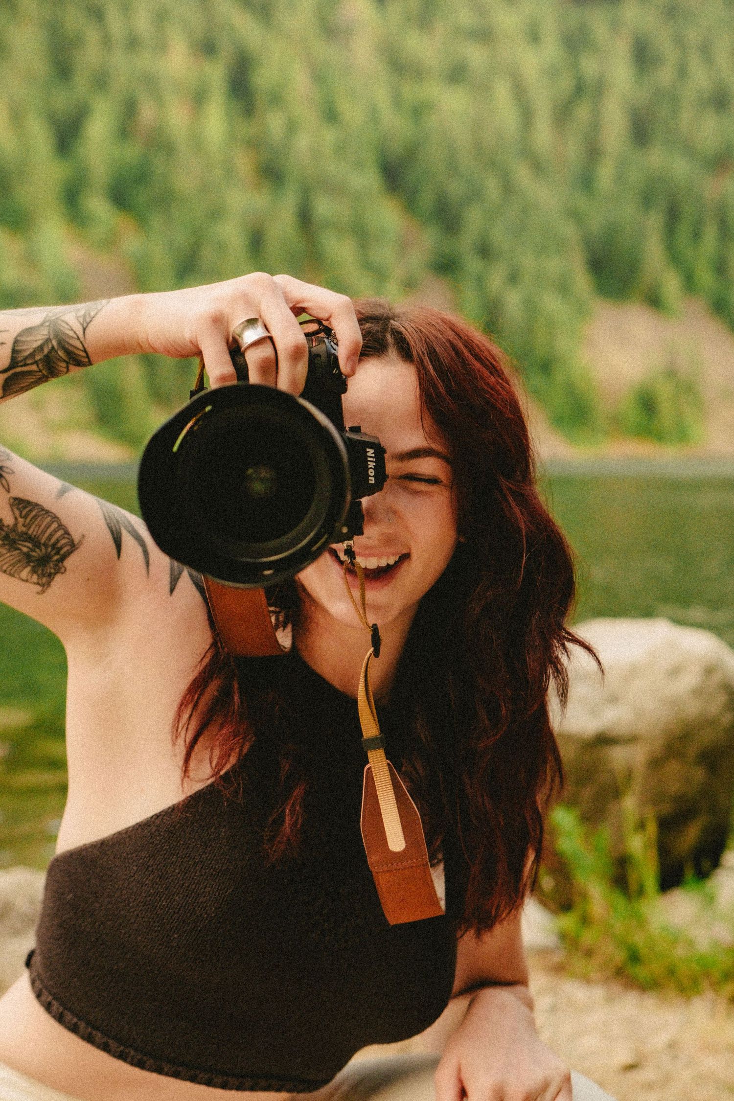Photographer with long dark hair using professional camera by mountain lake in warm summer lighting.