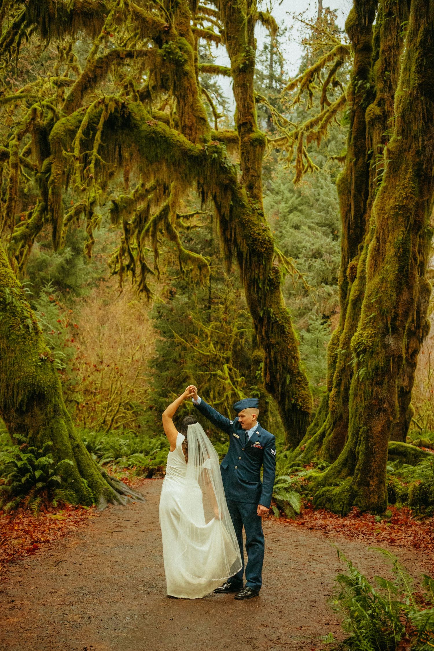 A couple shares a romantic wedding dance moment on a forest path surrounded by towering moss-covered trees in the Pacific Northwest.