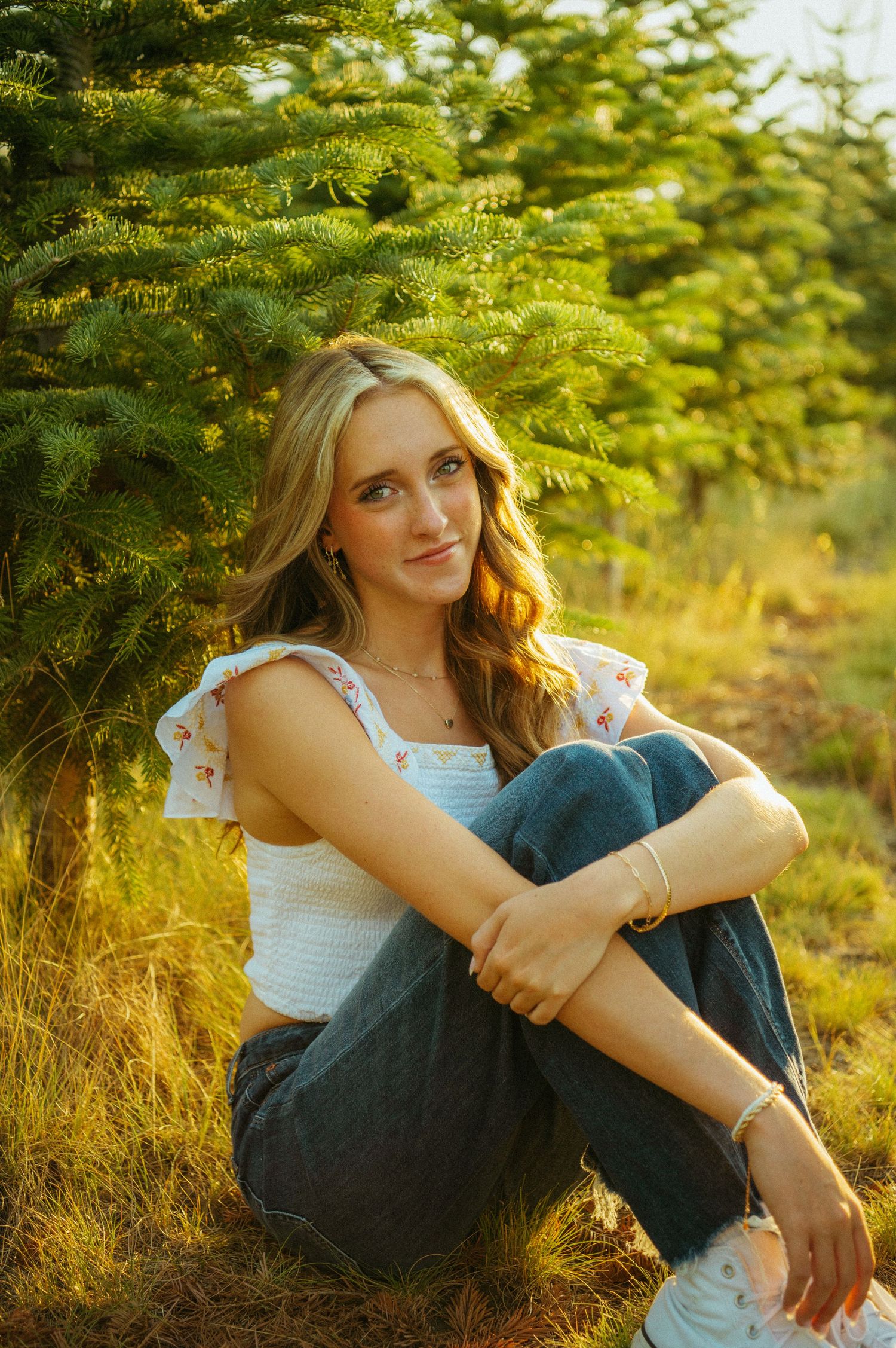 A dreamy summer portrait in golden light with evergreen trees and tall grass in a natural outdoor setting.