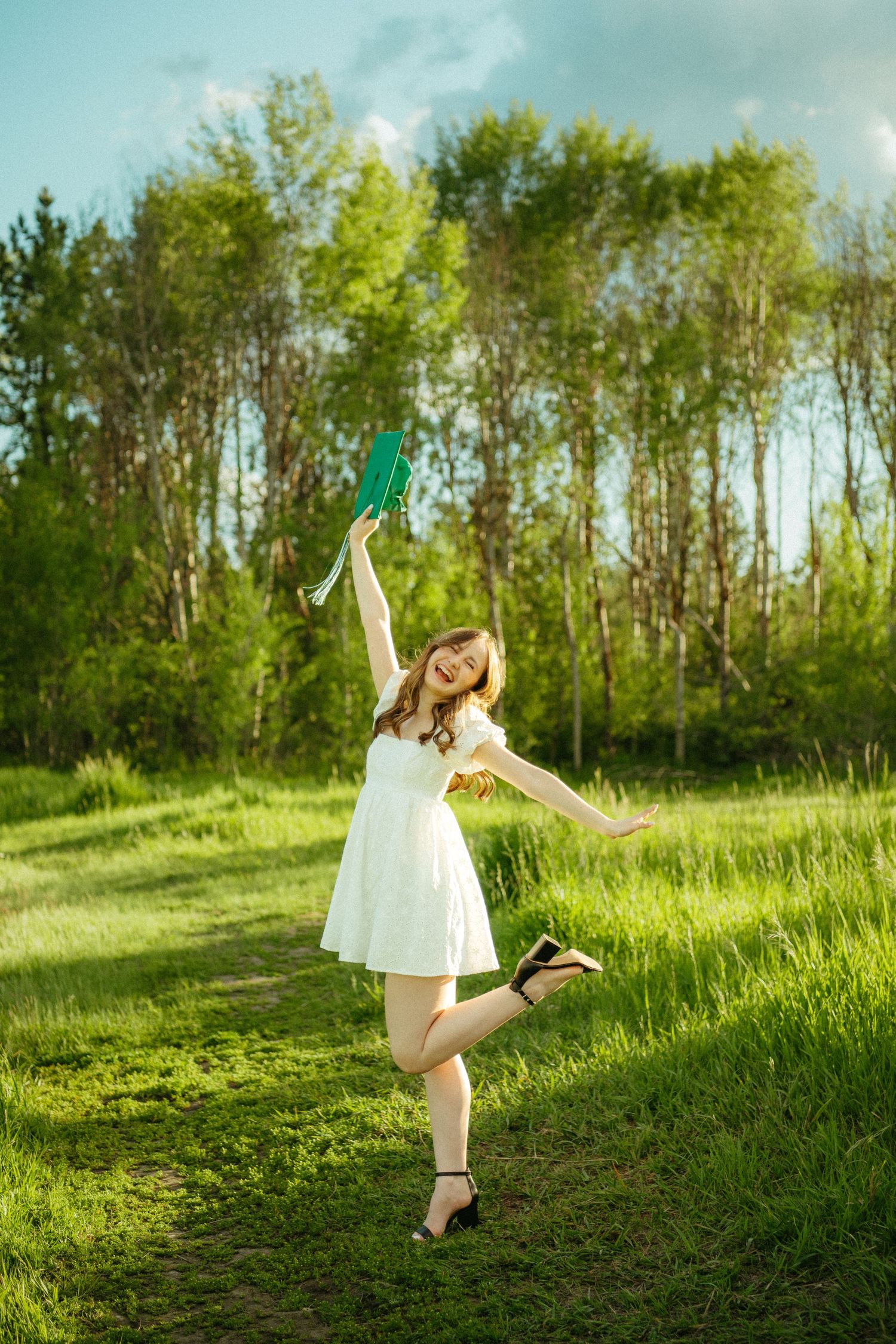 A dancer in a white dress performs graceful movements on a grassy hillside surrounded by trees in golden sunlight.