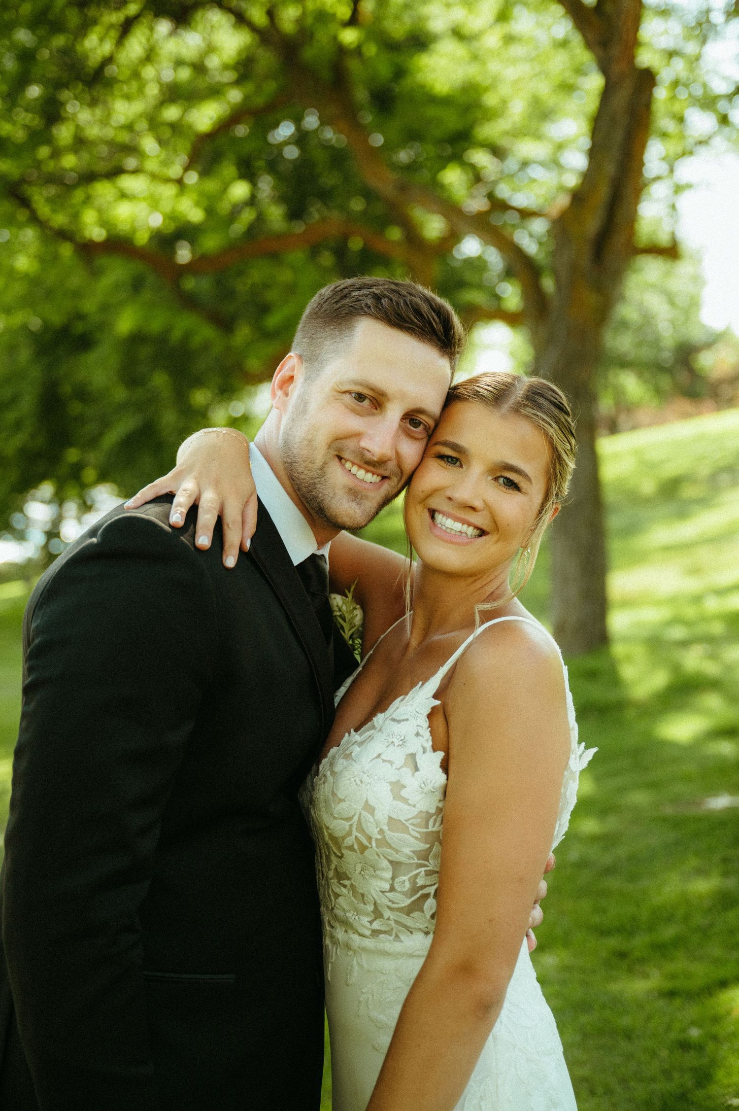 A couple in wedding attire embraces outdoors in a lush green garden setting during their special day.