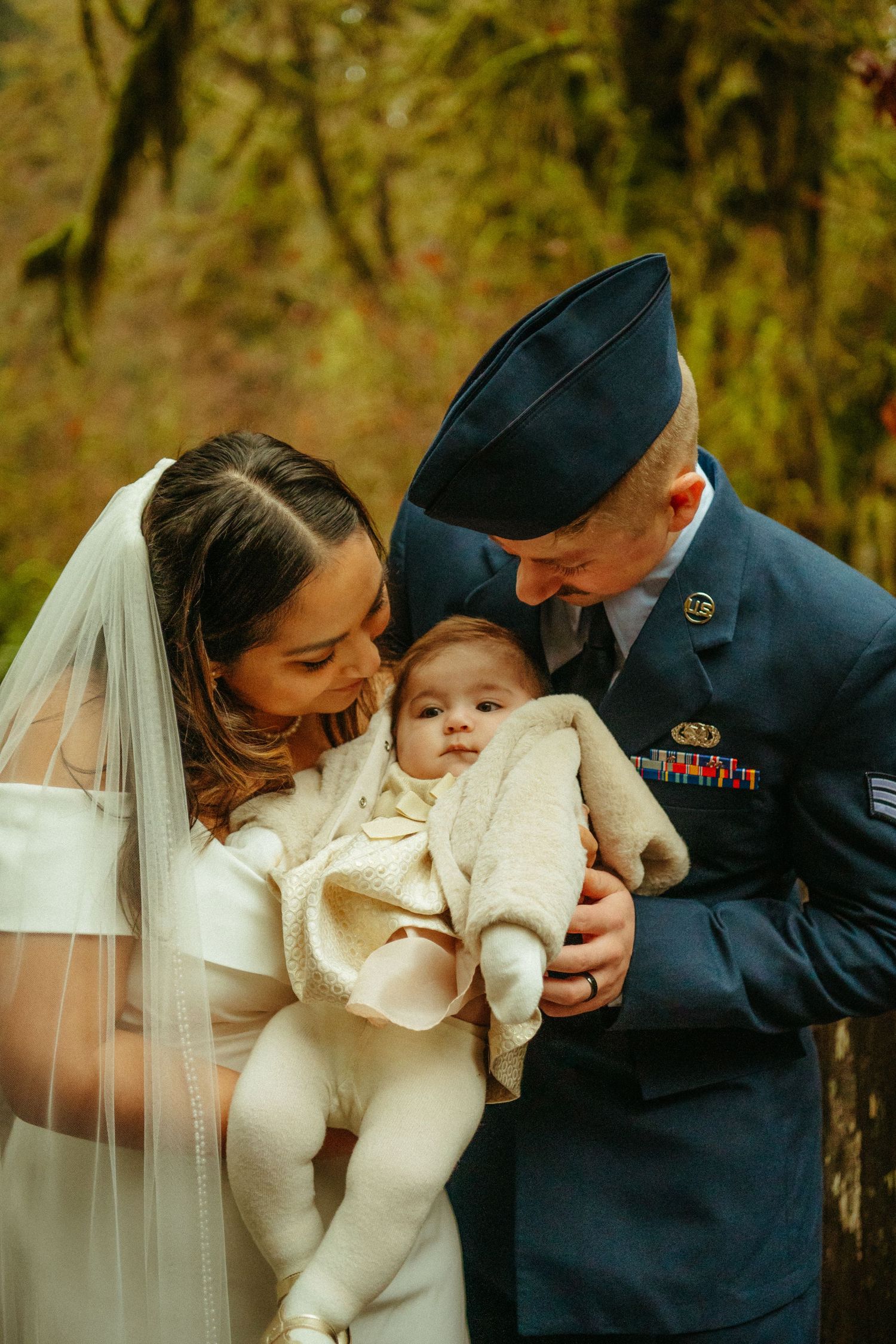 A tender wedding moment captured in autumn with a couple in dress whites and military uniform holding a small baby.
