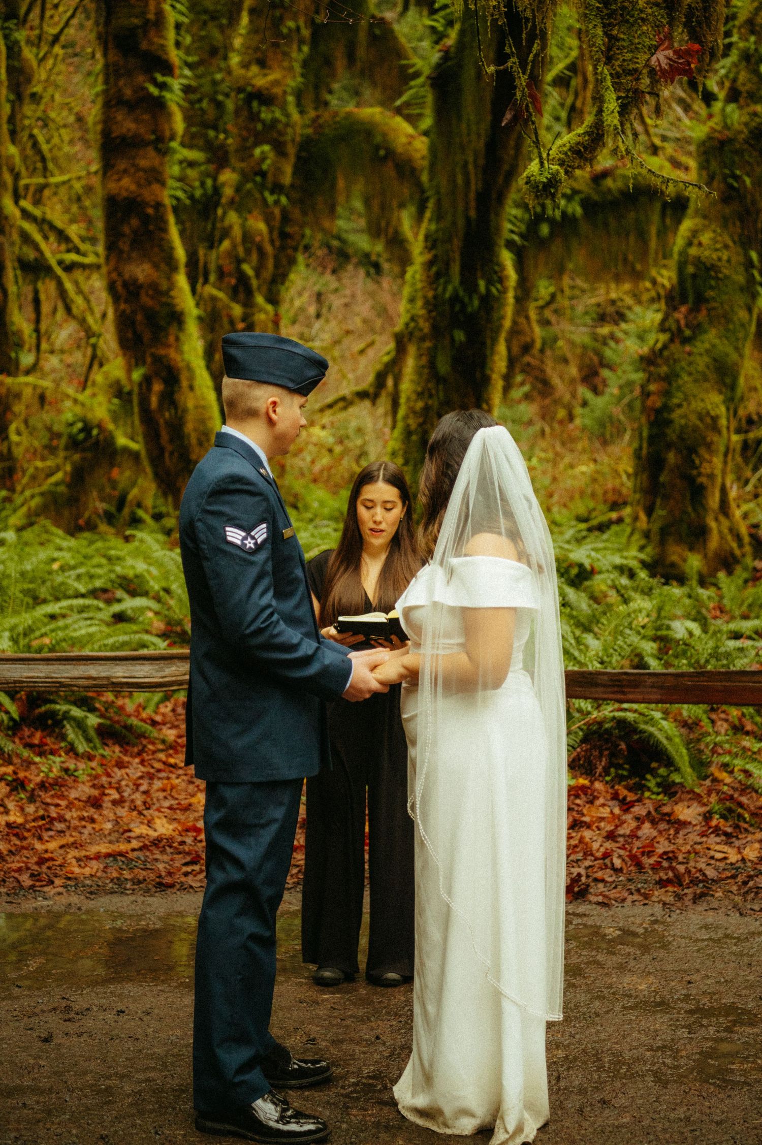 A military wedding ceremony takes place in a mossy forest setting with an officiant performing the service.