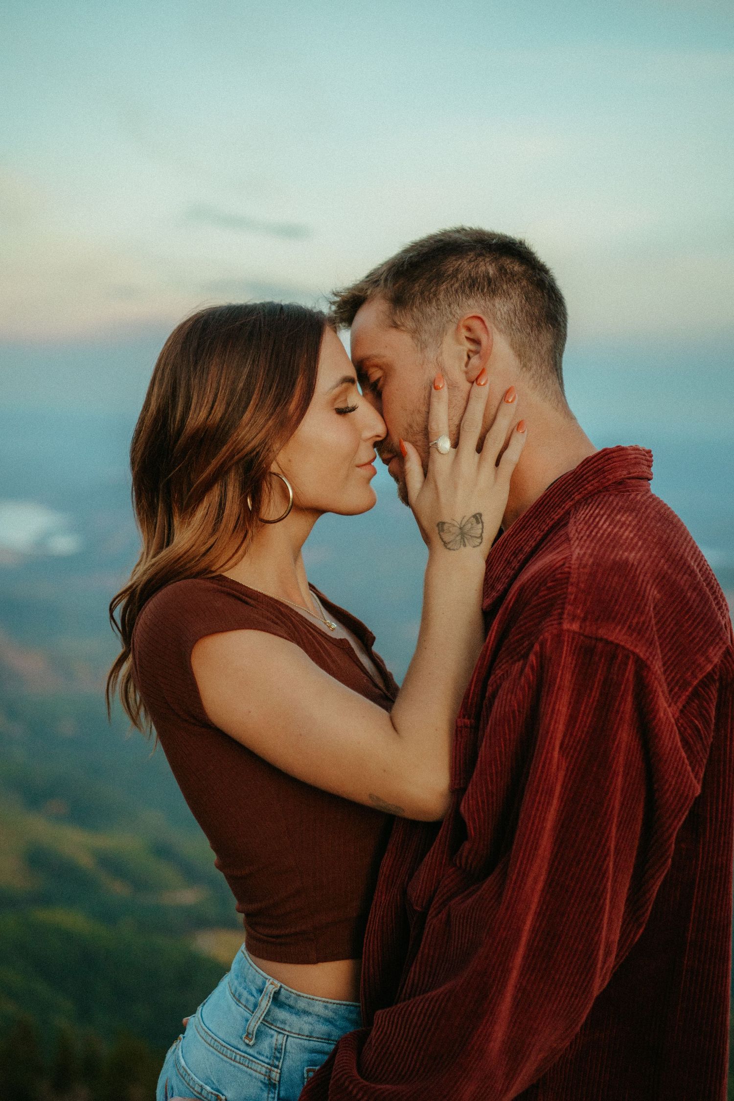 A romantic couple sharing an intimate moment at sunset against a mountainous landscape backdrop.