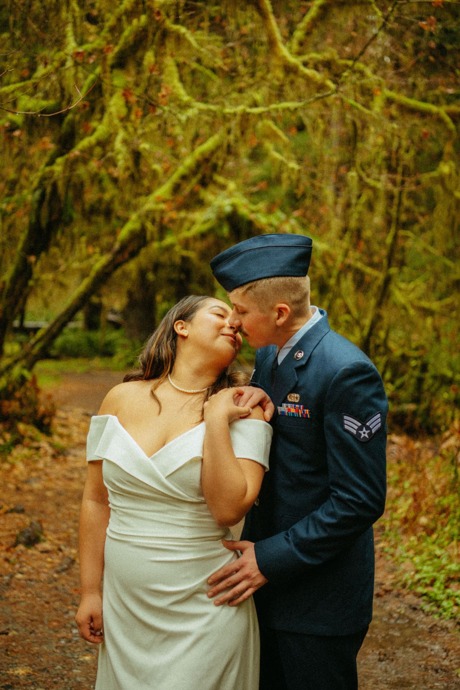 A couple shares an intimate moment in their wedding attire surrounded by autumn forest scenery.