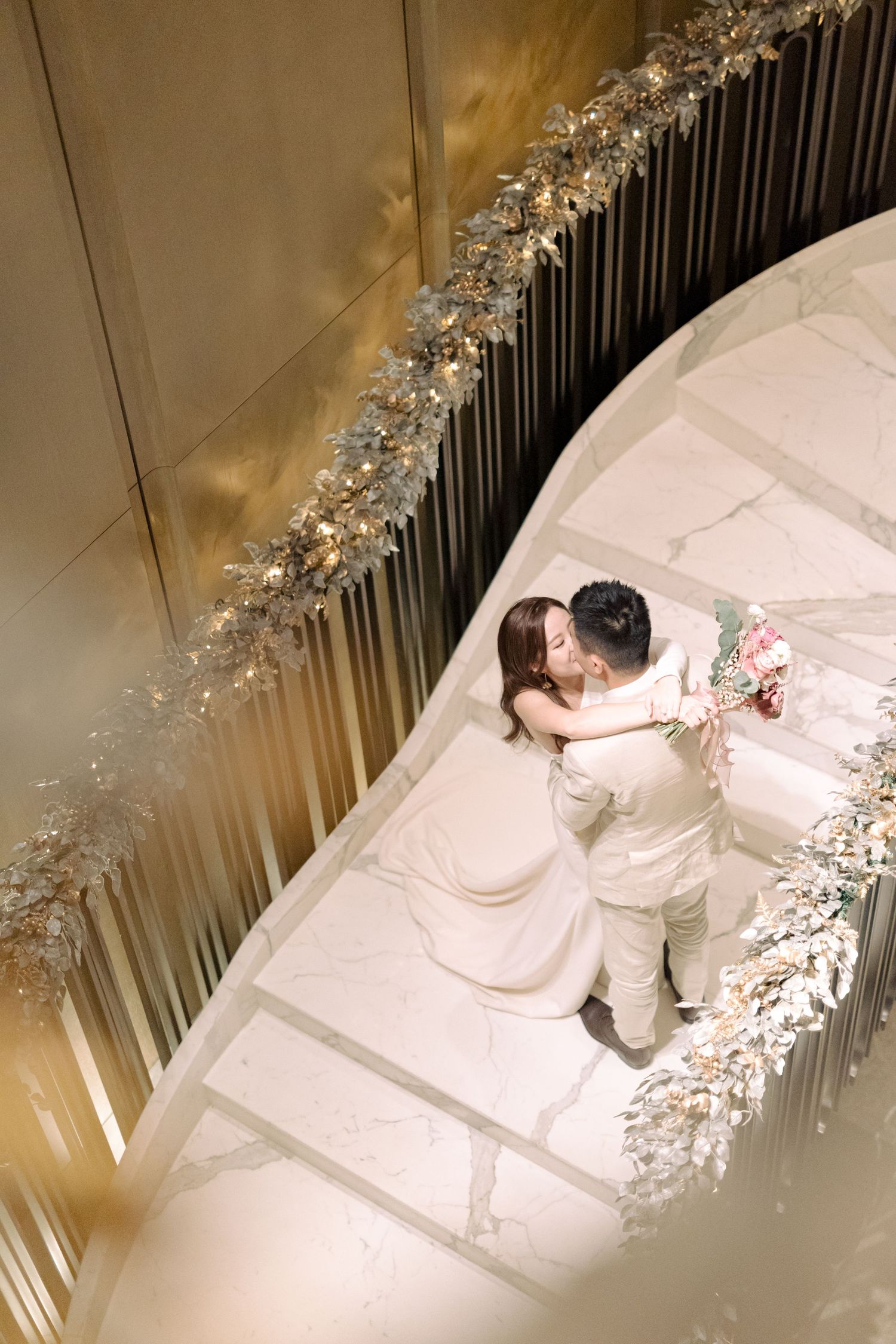 Aerial view of a couple embracing on a white staircase decorated with elegant crystal and floral arrangements.