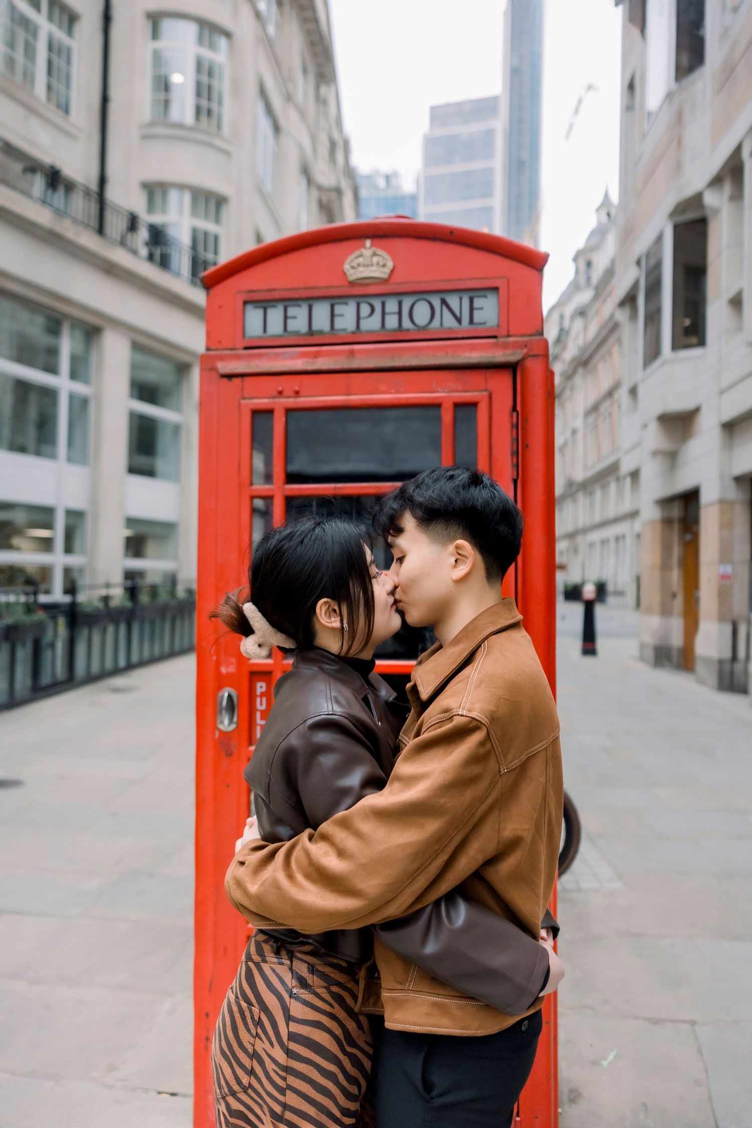 Couple embracing and almost kissing in front of iconic red London telephone box on a city street.