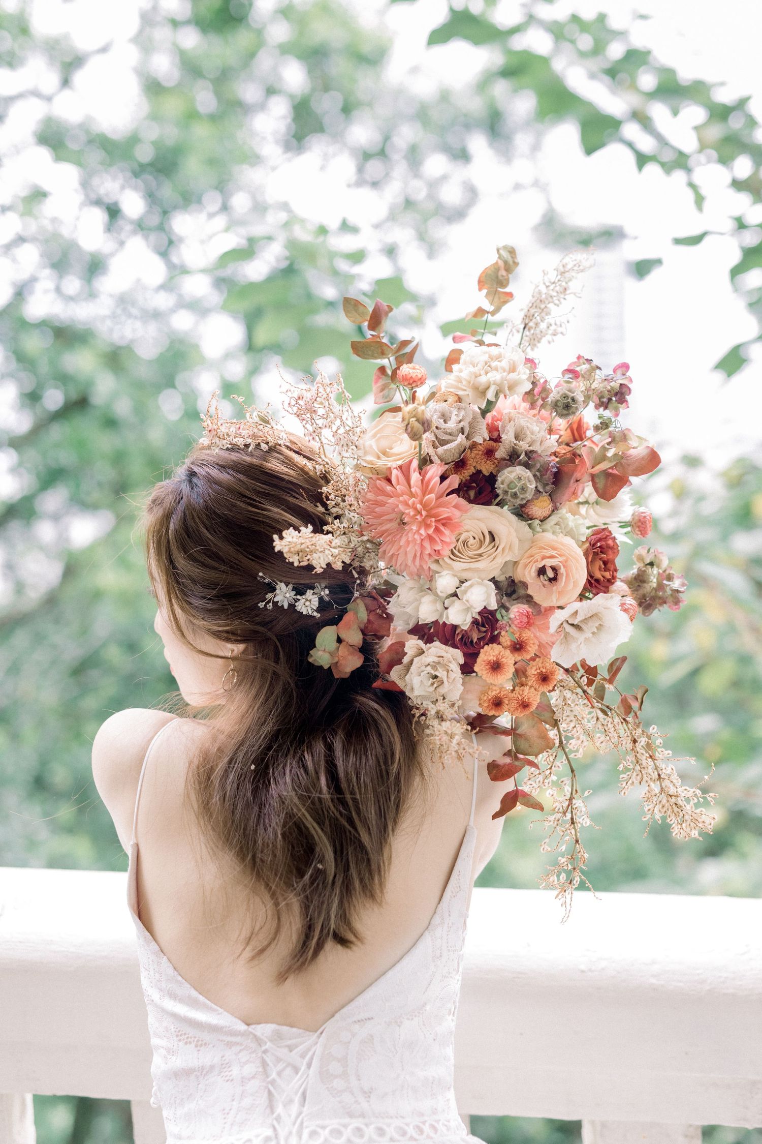 A delicate floral hair accessory featuring dried flowers in peach and blush tones adorns an upswept hairstyle.