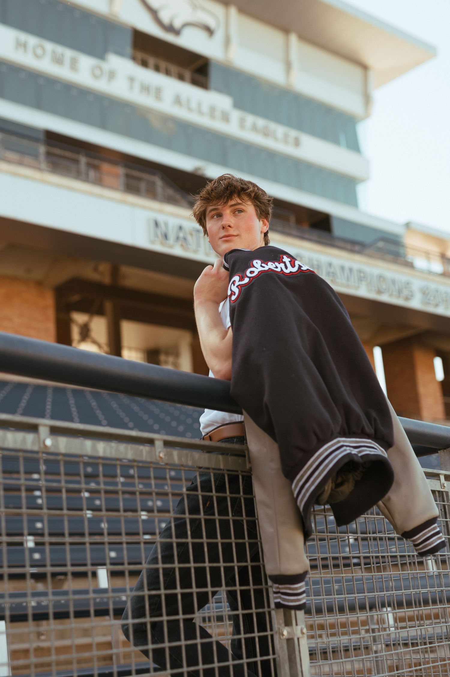 A person in casual athletic wear leans against a railing outside a building in warm sunset lighting.
