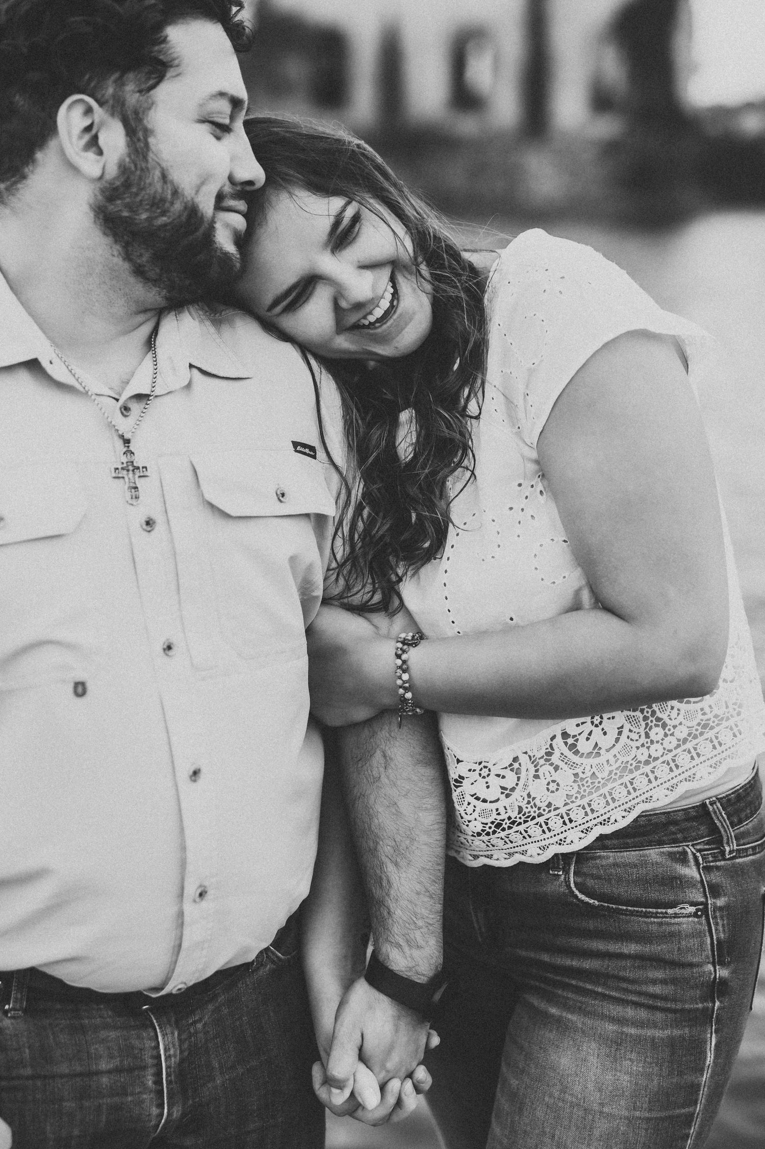 Black and white photo of a smiling couple holding hands and leaning together affectionately outdoors.