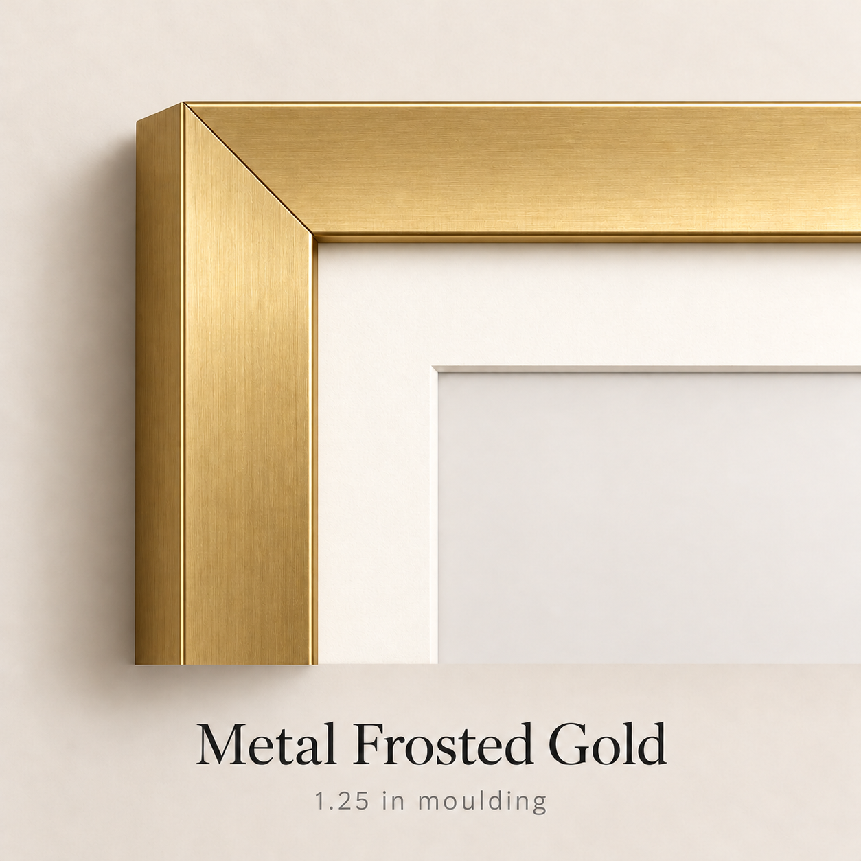 Close-up corner of a metal frosted gold picture frame with 1.25 inch moulding and a white mat against a soft neutral wall.