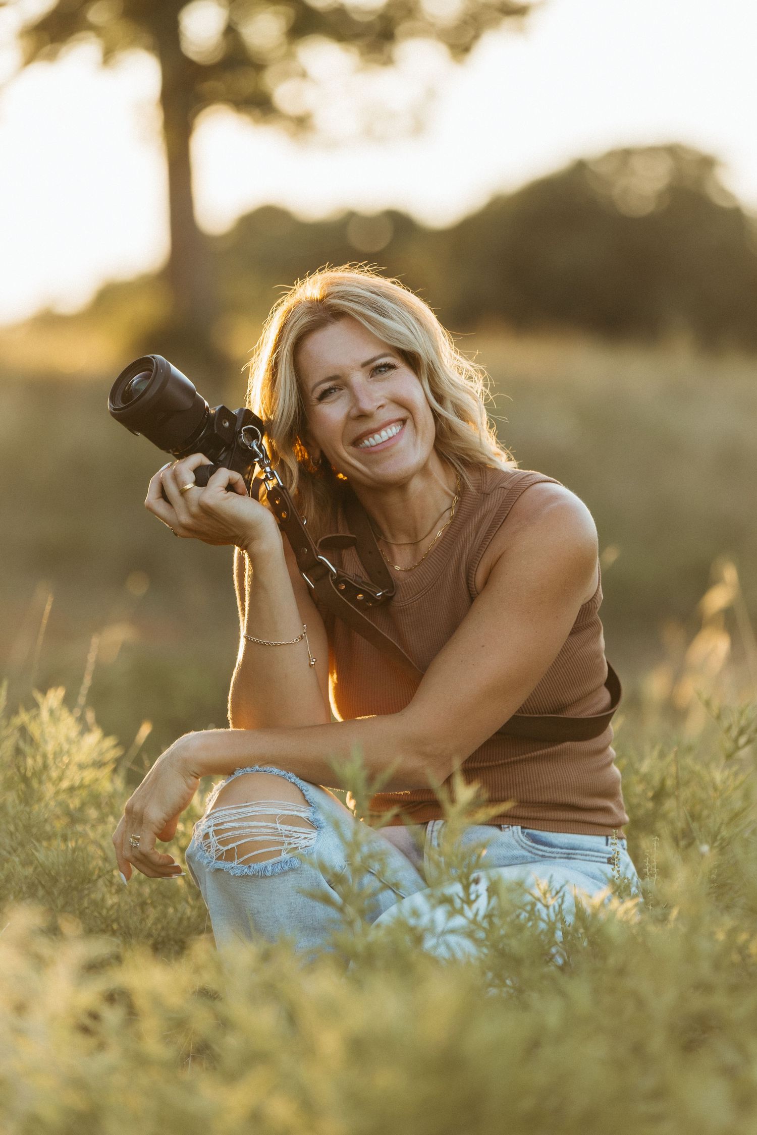 Photographer lying in grass during golden hour captures images with professional camera while smiling.
