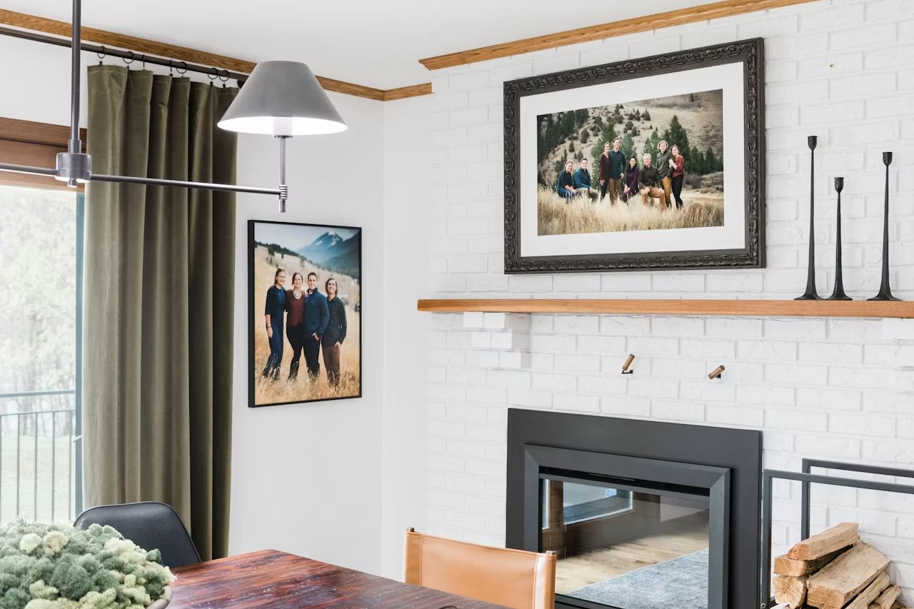 Cozy living room with white brick fireplace, wood mantel, family photos, pendant light, and rustic dining table.