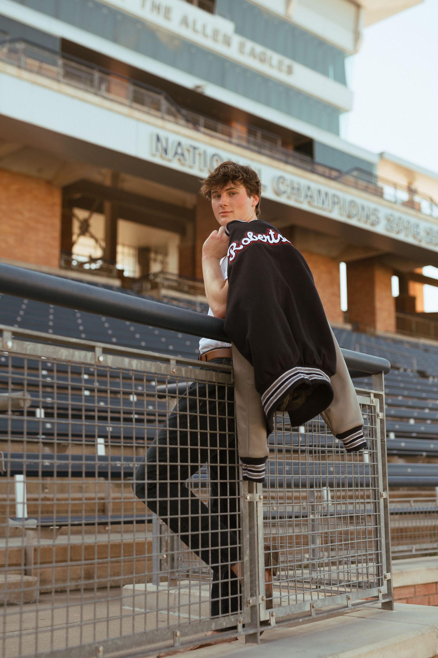 Person in black athletic wear sits perched on metal railing at empty stadium during golden hour.