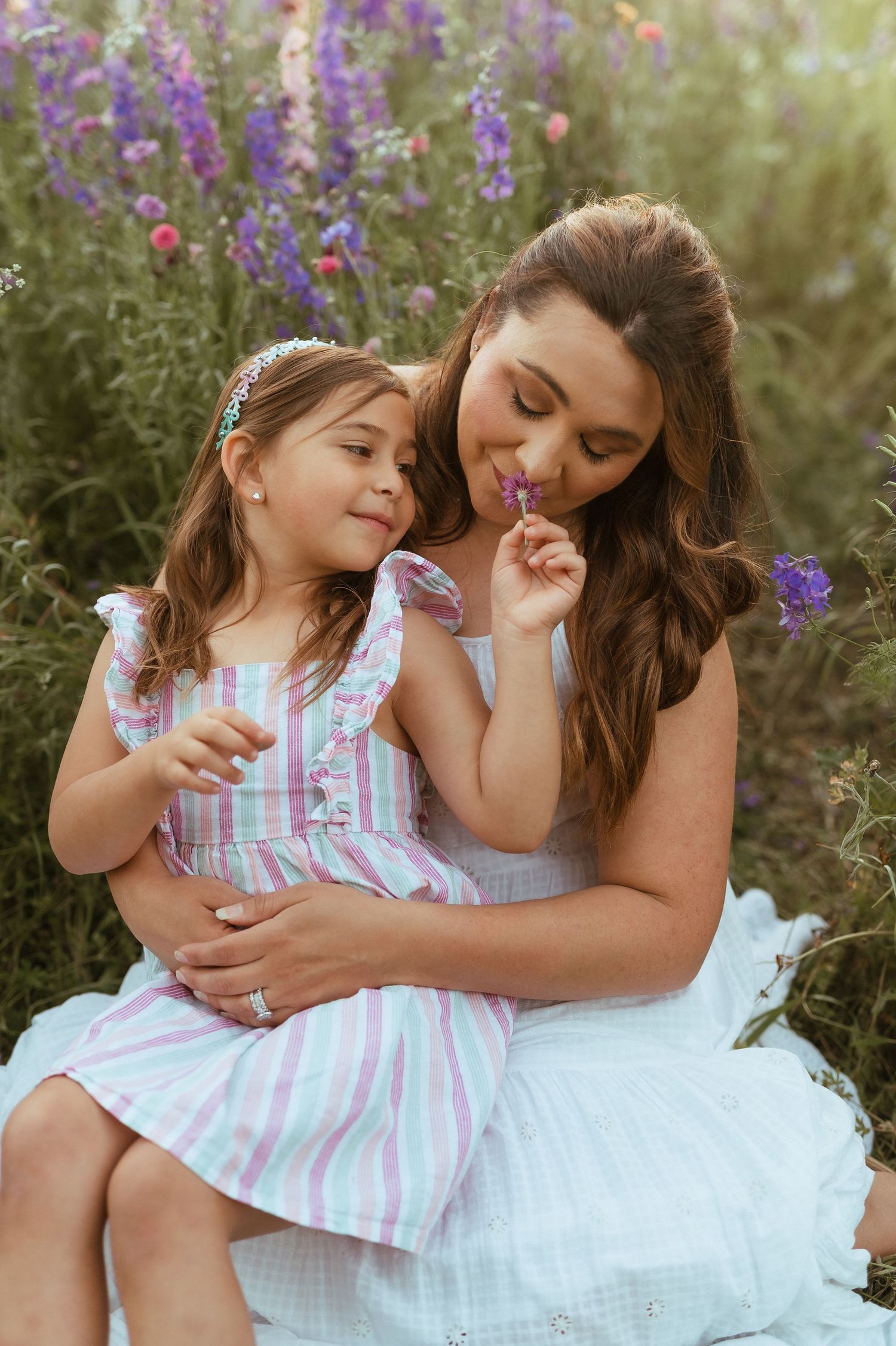 Two people share a tender moment while sitting outdoors among purple wildflowers on a sunny summer day.