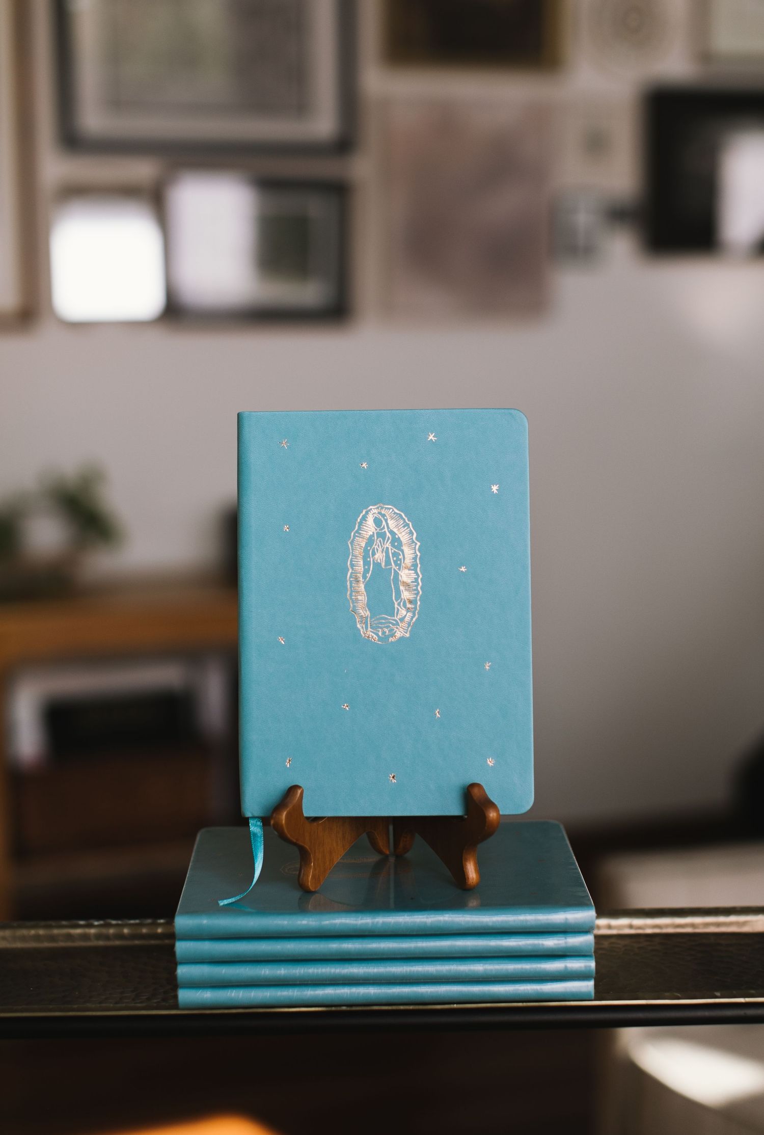 Stack of light blue notebooks with decorative design displayed on wooden stand.