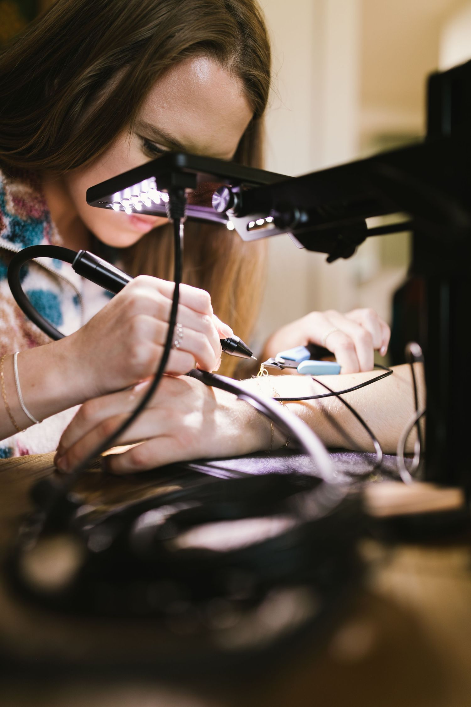Close-up view of hands working with precision tools and welding materials at a crafting desk.