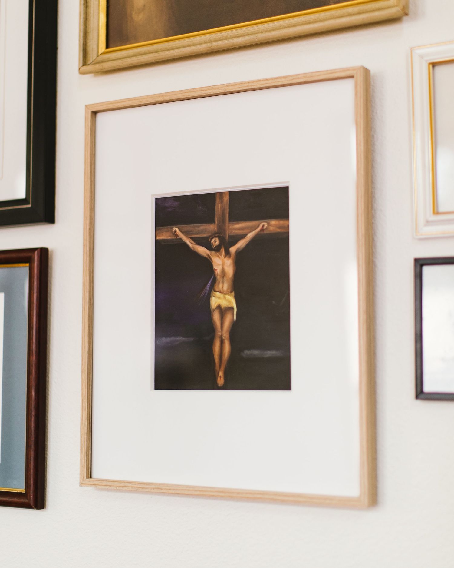 Framed photograph of a crucifix mounted on a wall alongside other artwork in gold and black frames.