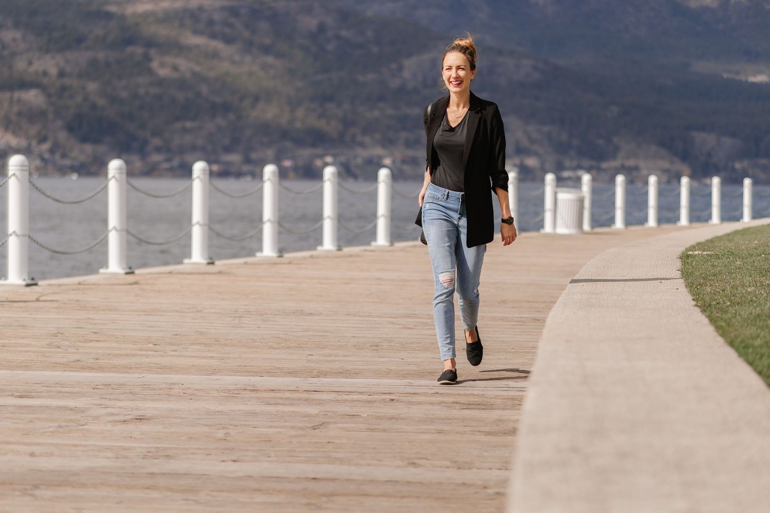Person walking their dog along a scenic waterfront path with mountains and water views in the background.