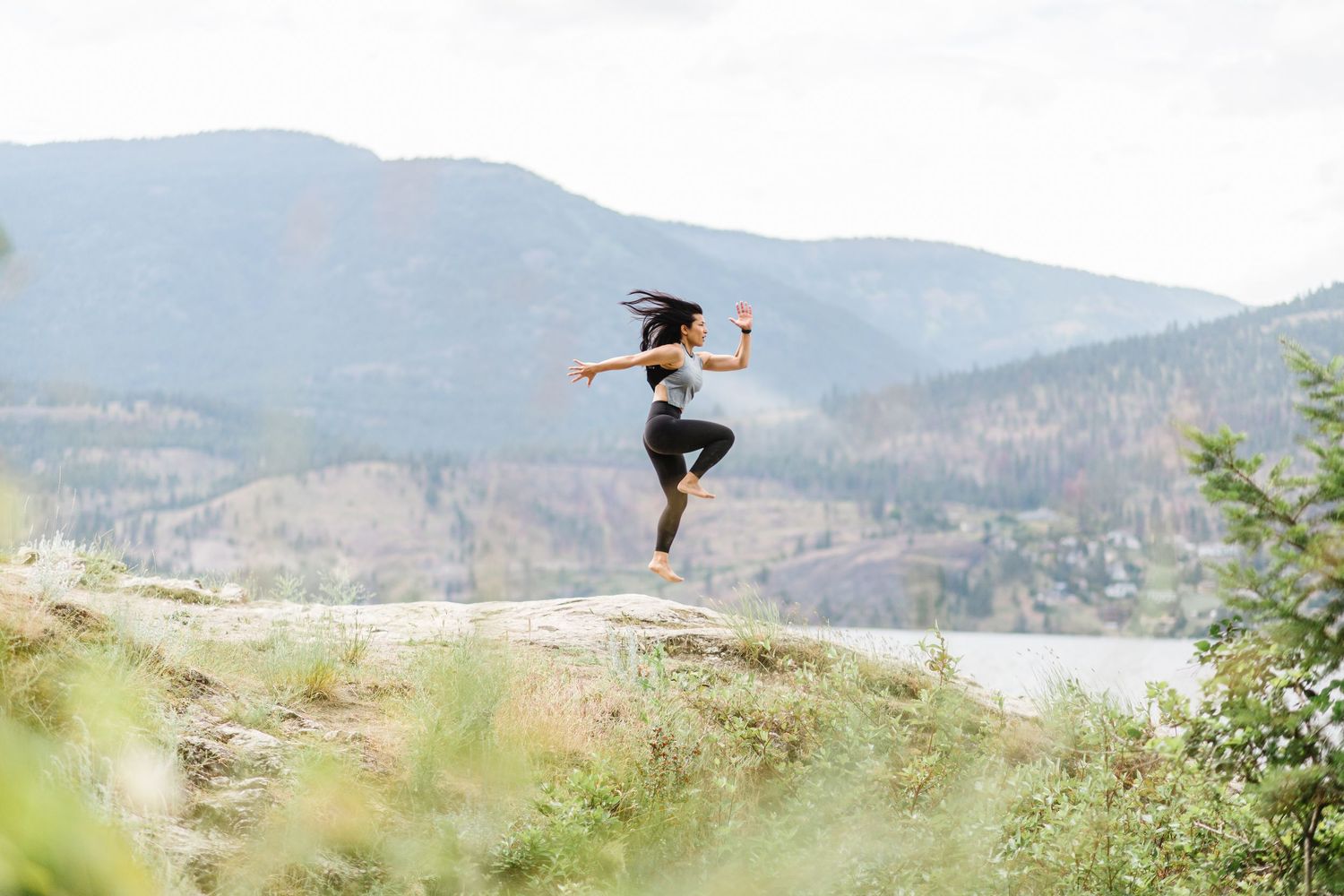 A person performs an impressive jump trick on a mountain bike against a scenic mountain landscape backdrop.