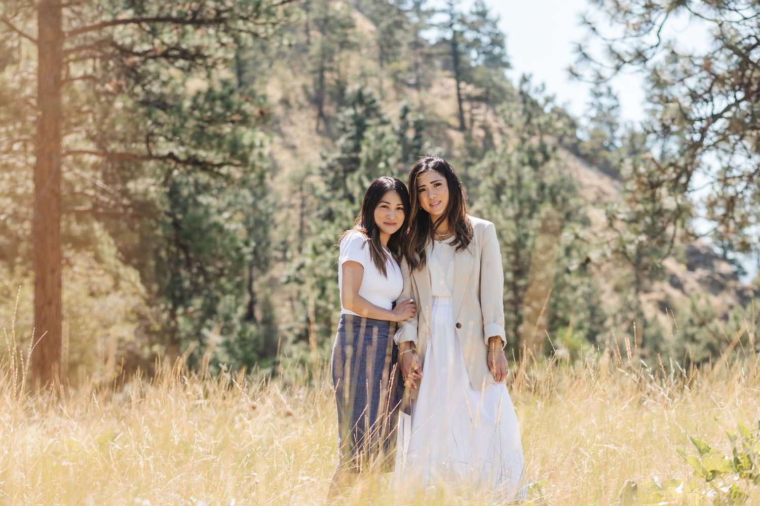 Family members in coordinated white outfits sit together on rocky terrain with mountains and trees in background.