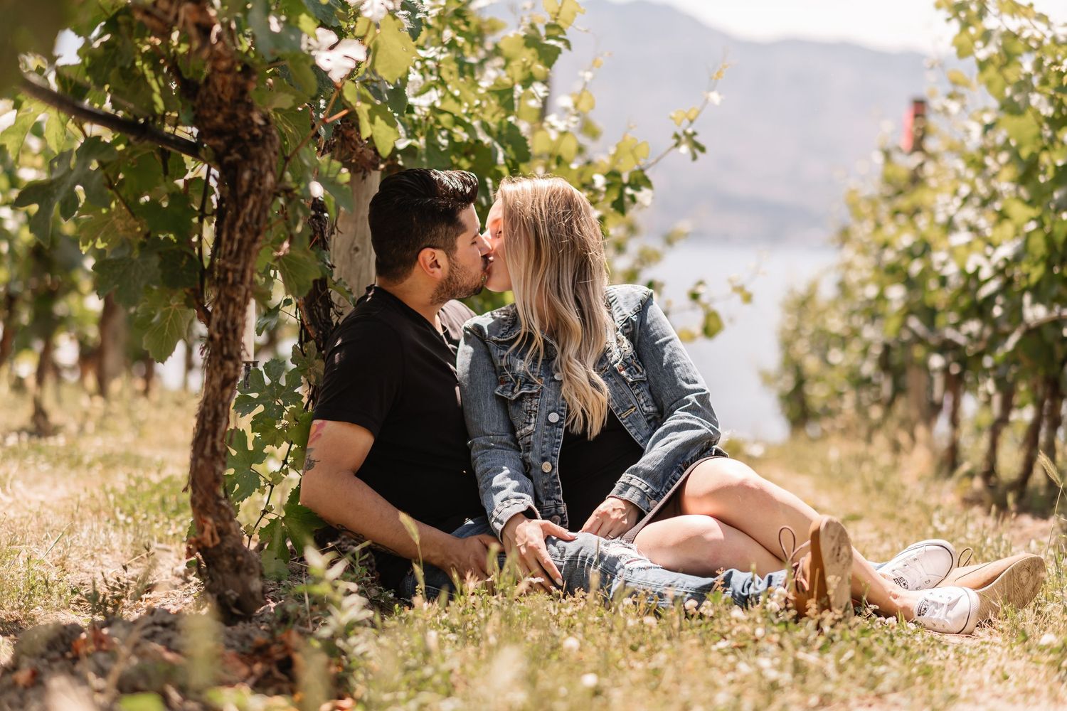 A romantic couple shares tender moments in a sunlit vineyard with mountains in the background.