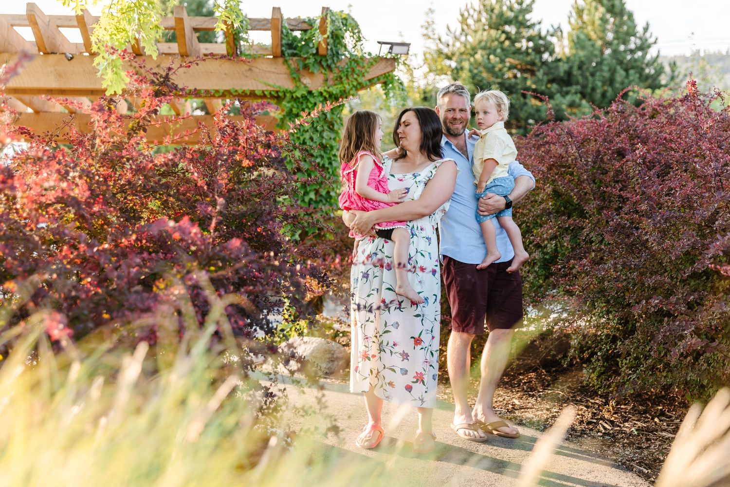 Family poses together in a garden setting with beautiful fall foliage and warm sunlight during golden hour.