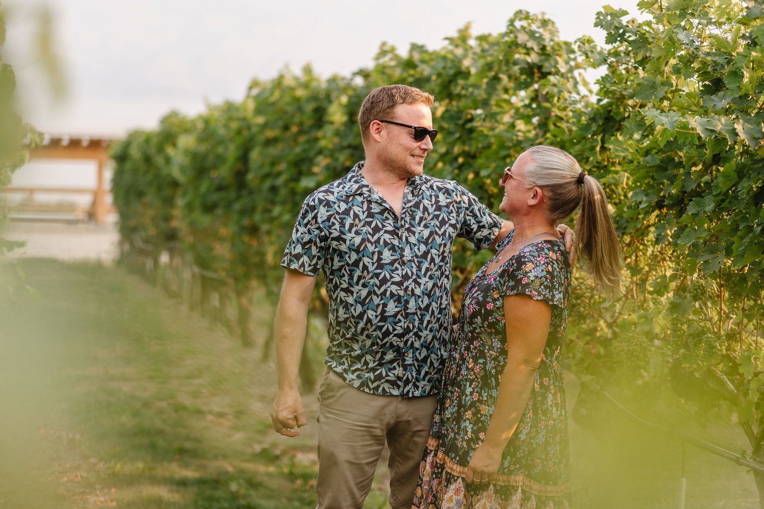 A couple shares a joyful moment together while walking through a lush vineyard on a sunny afternoon.