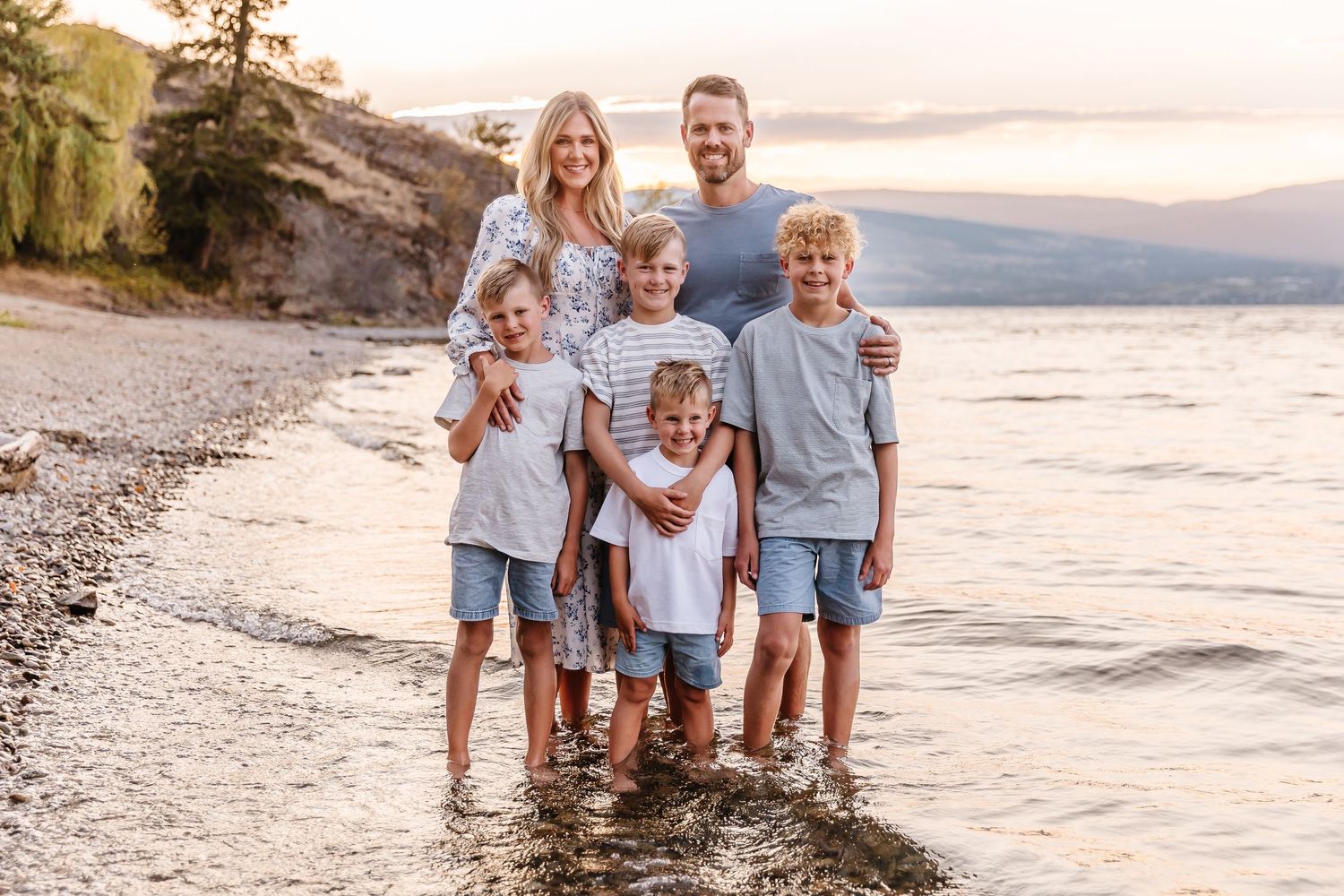 A group wearing coordinated blue and white outfits poses together on a scenic beach at sunset.