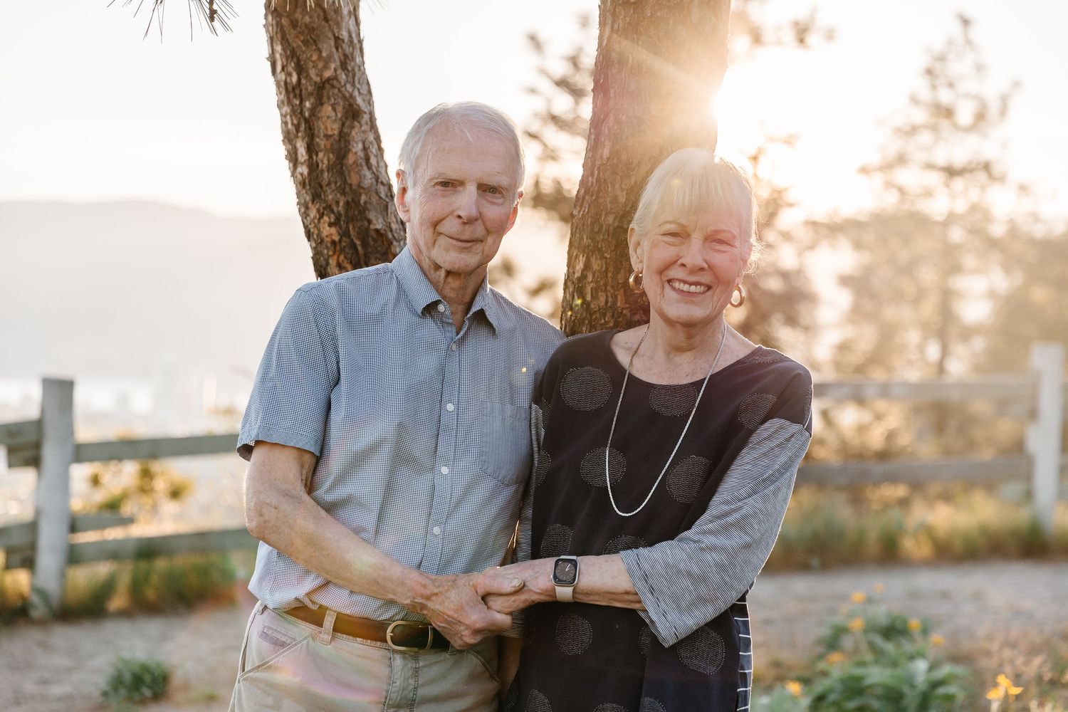 A couple sits together outdoors during golden hour sunlight, sharing warm smiles and embraces in nature.
