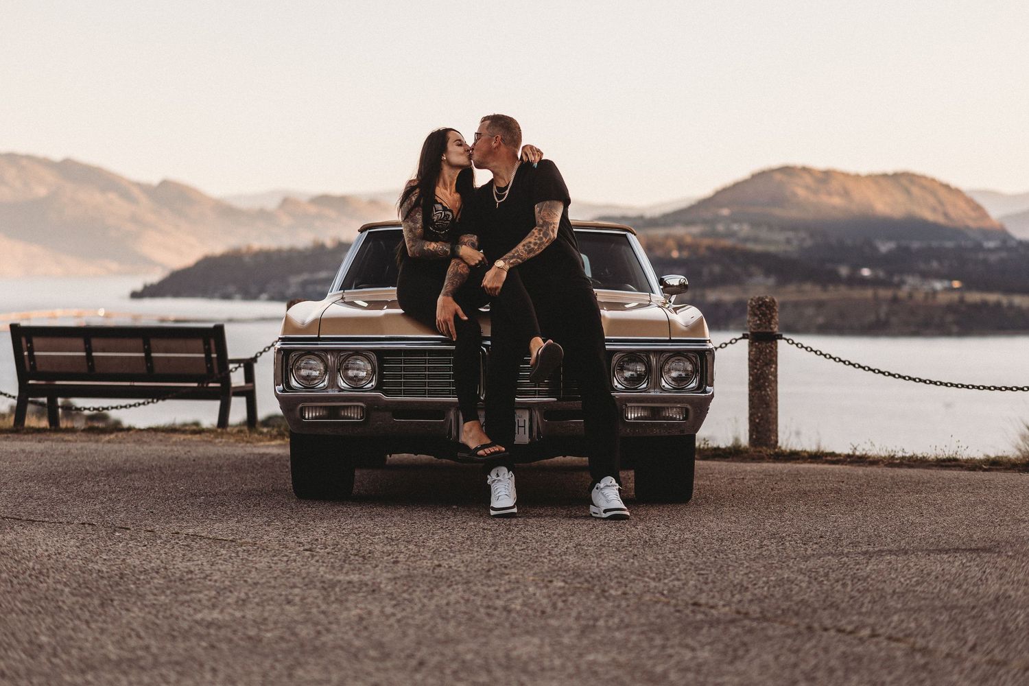 A couple sits on a bench at sunset overlooking a serene mountain lake in a romantic setting.