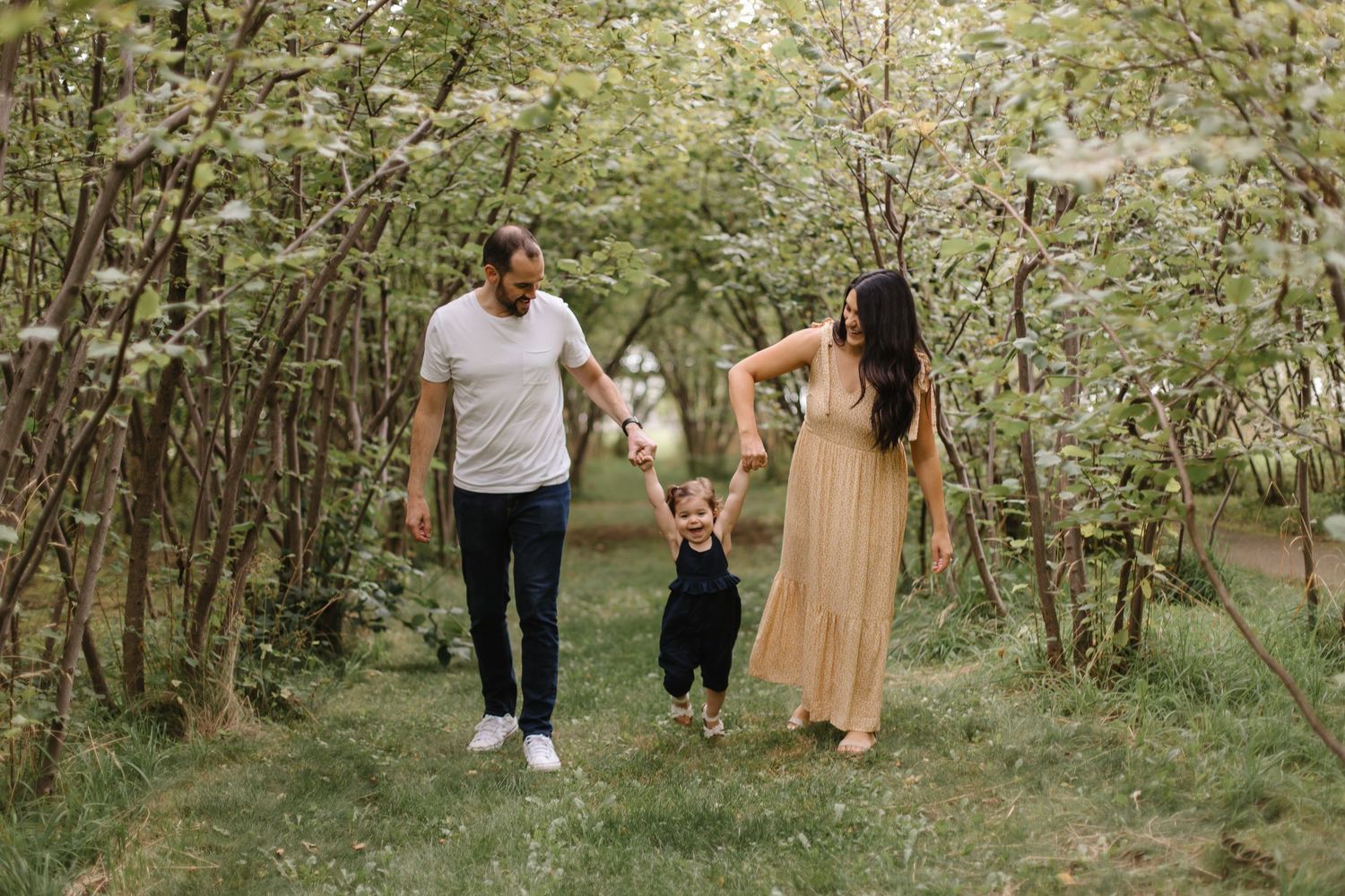 A family walks together through a lush green forest path on a sunny afternoon.