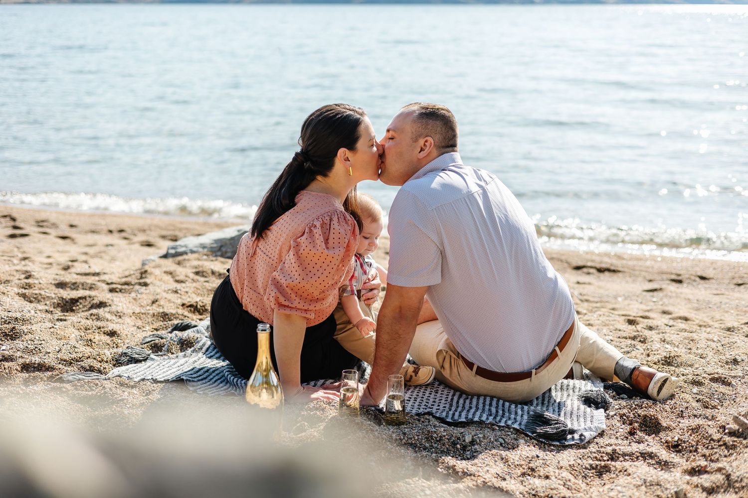 Romantic couple sharing an intimate moment while sitting on a sandy beach with ocean waves in the background.