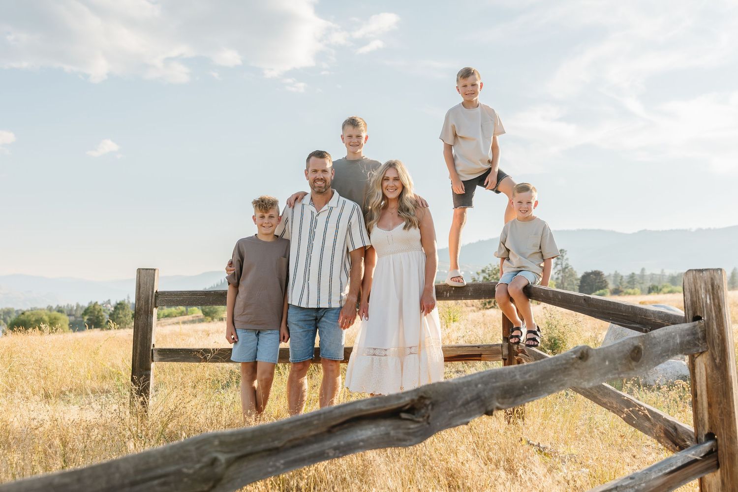 A group of people stand together in a golden wheat field at sunset against a mountain backdrop.